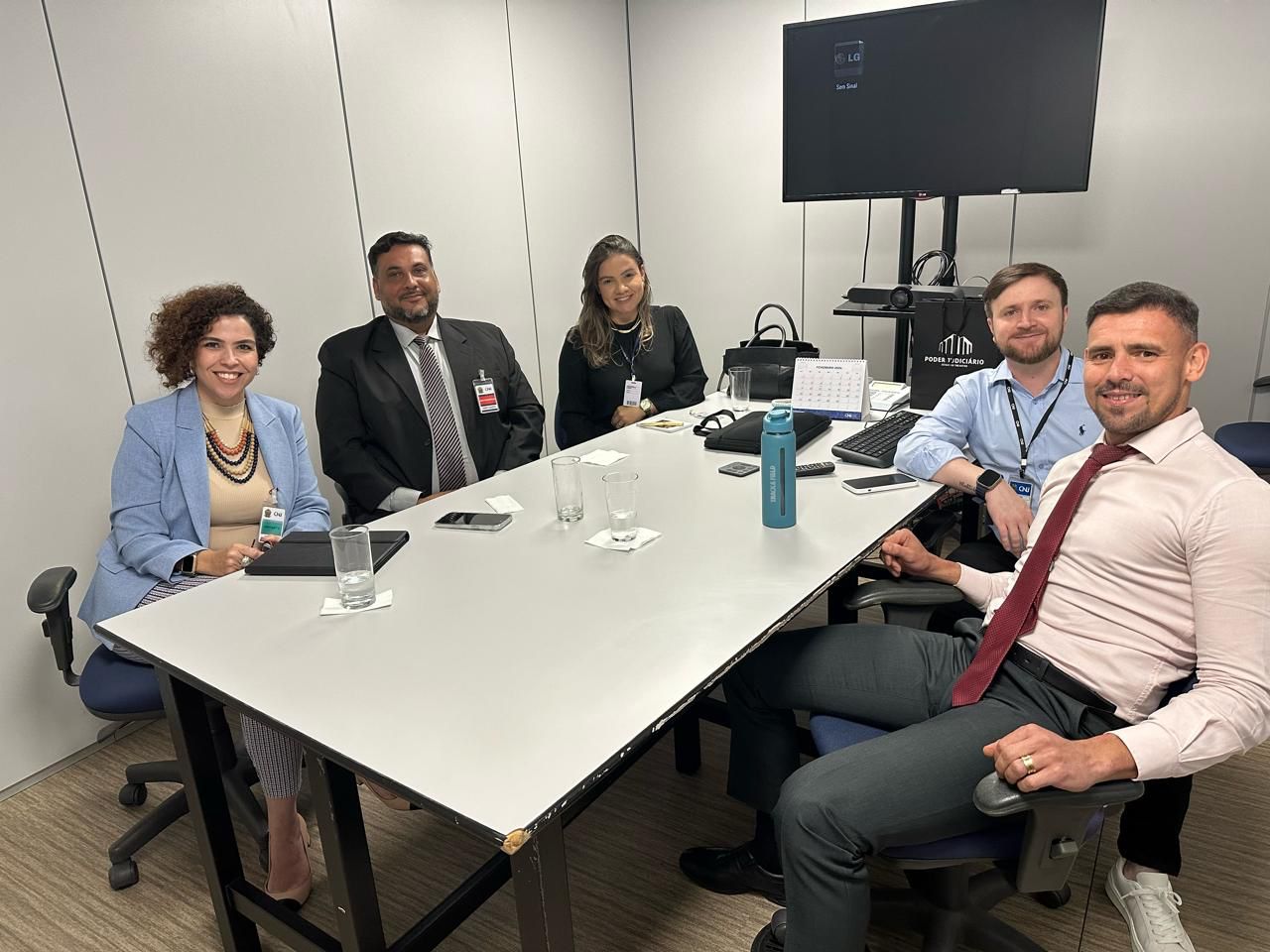 Fotografia colorida onde três membros da equipe gestora do Projeto Passando a Limpo  estão sentados em uma mesa no CNJ com os chefe da Divisão de Gestão Estratégica do CNJ, Adilson Medeiros da Silva; e o chefe da Seção de Estudos Organizacionais e Normas do CNJ, David Cosme Alves Pereira.
