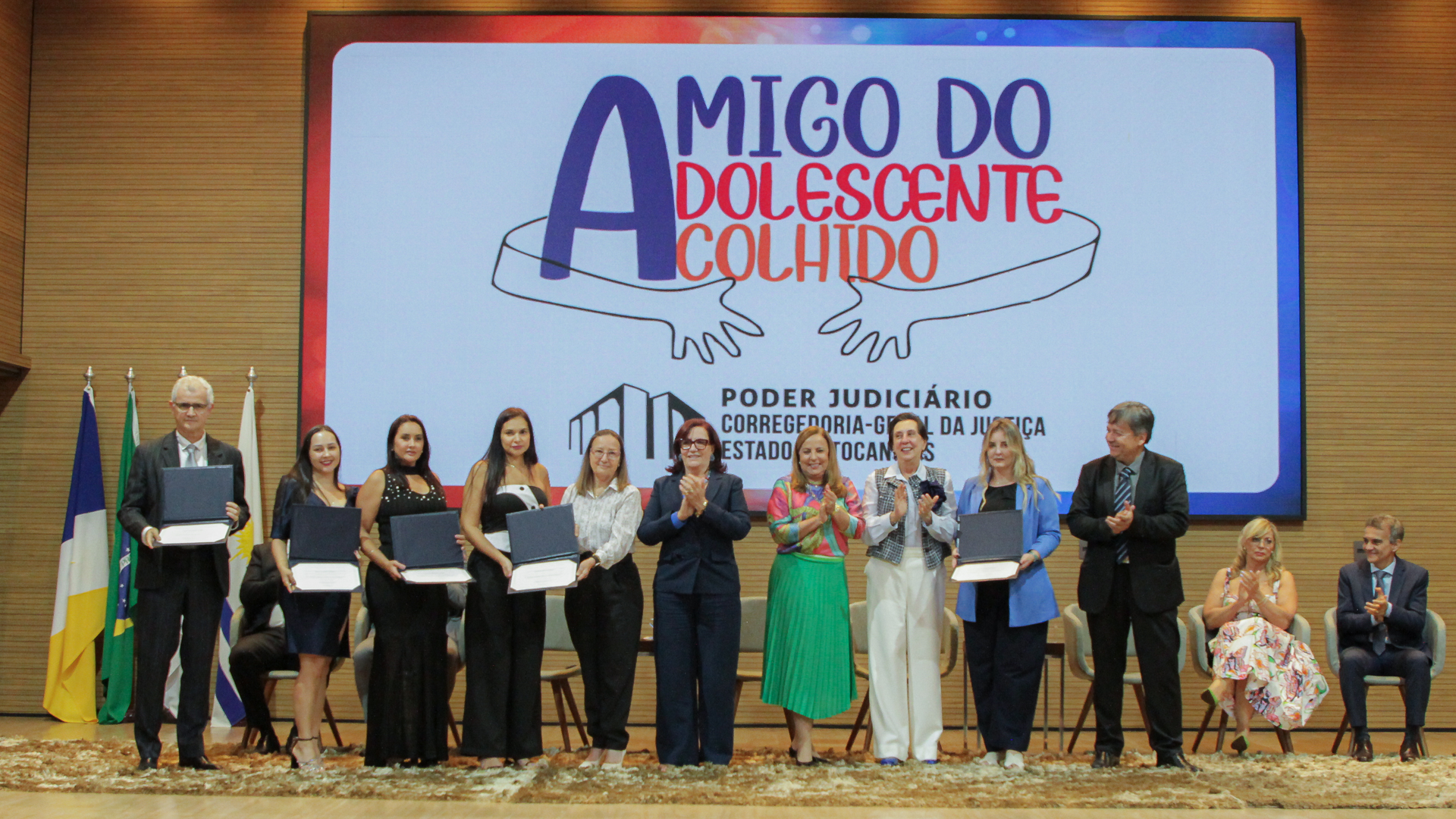 Fotografia colorida de um grupo de empresários junto com representantes do tribunal de justiça recebendo o prêmio de reconhecimento "Amigo do adolescente acolhido" 