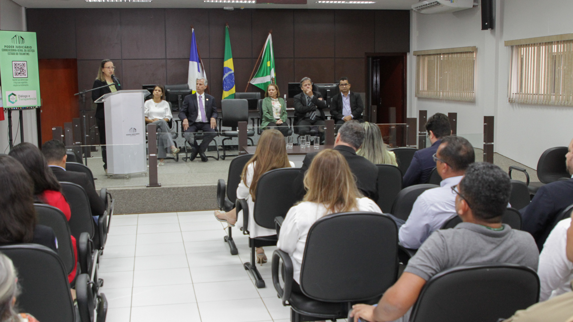 Fotografia colorida onde a corregedora-geral da Justiça, desembargadora Maysa Vendramini Rosal fala apoiada em um palanque de madeira escura para um público sentado em cadeiras de um auditório 
