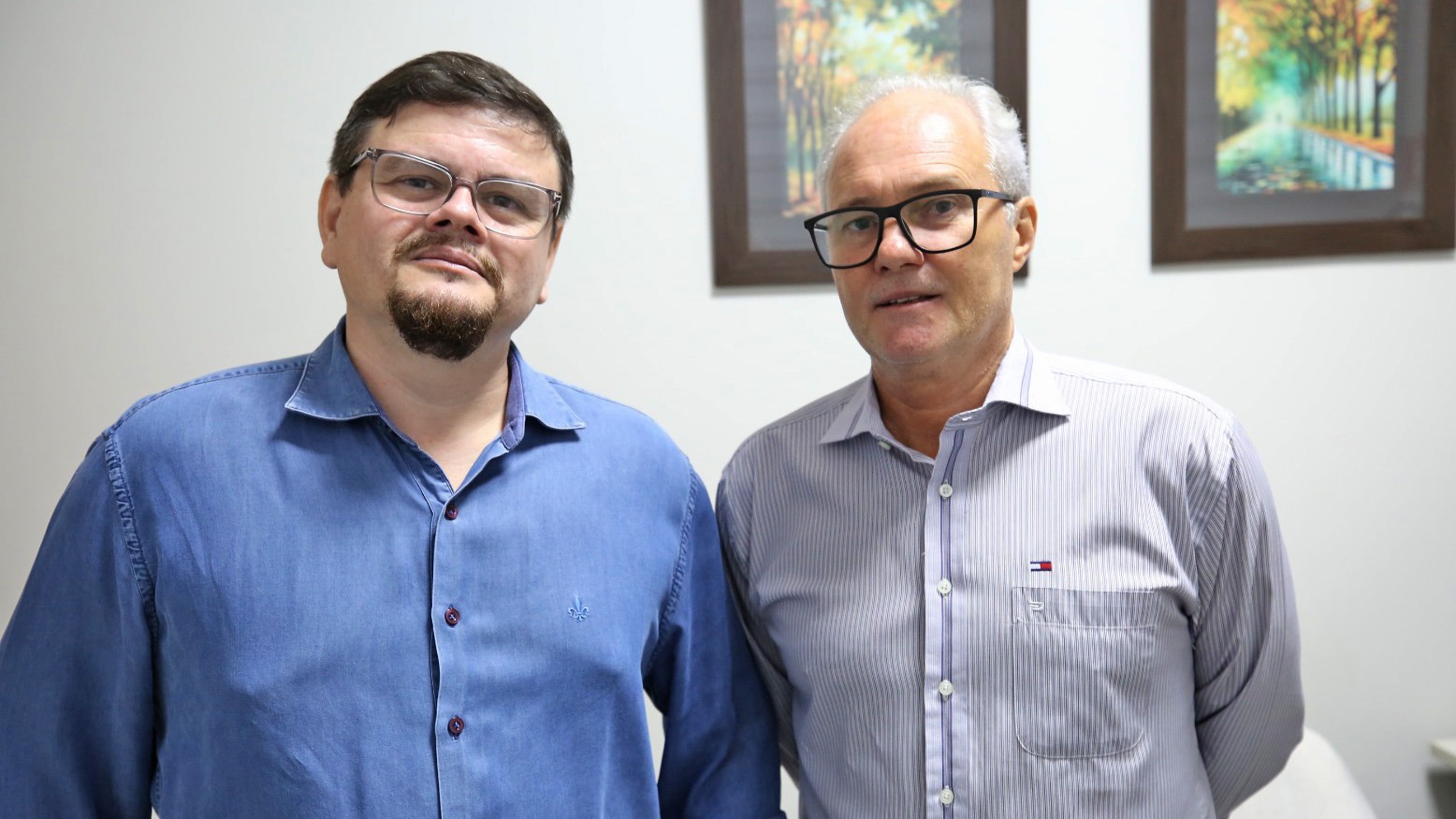 Imagem mostra dois homens brancos de óculos, com camisas em tons de azul pousando para fotos
