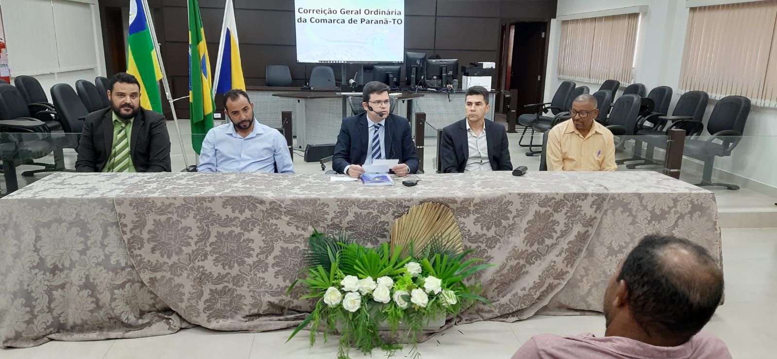 Fotografia colorida que mostra cinco homens sentados à mesa conversando