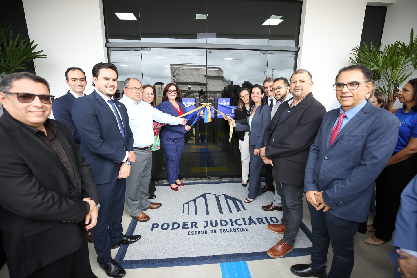 Fotografia colorida que mostra homens e mulheres desenlaçando fita de inauguração