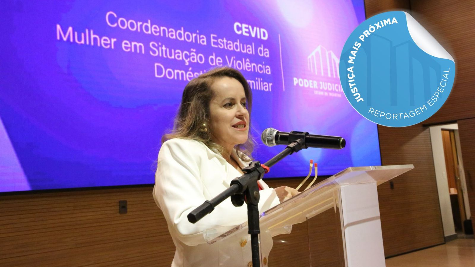 Fotografia colorida de uma mulher branca falando ao microfone