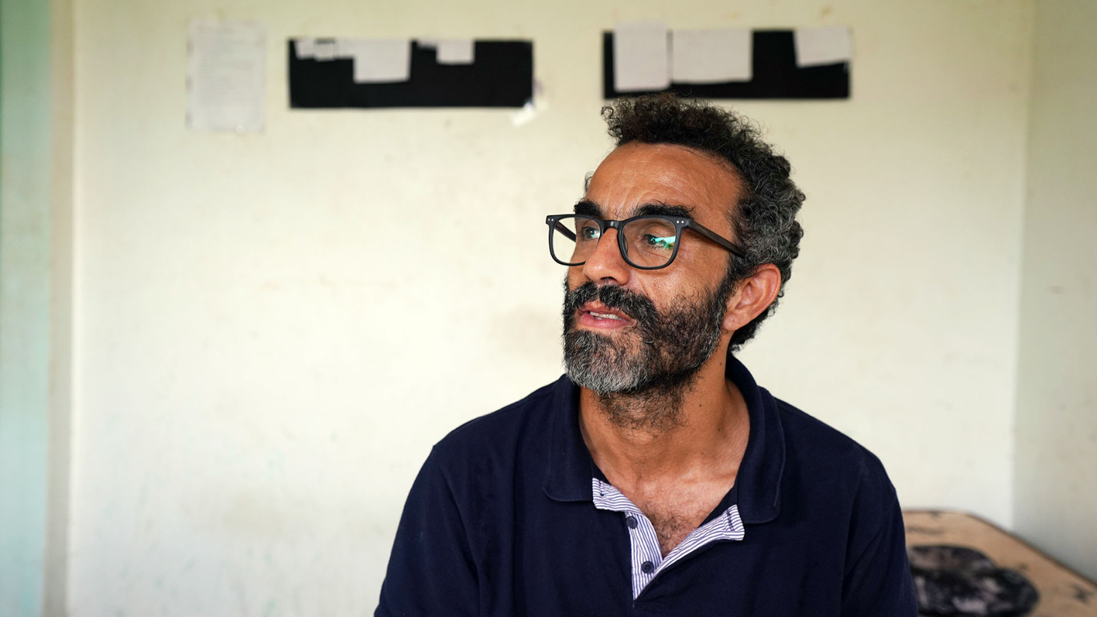 Homem barburdo e de óculos olha para o lado direito 