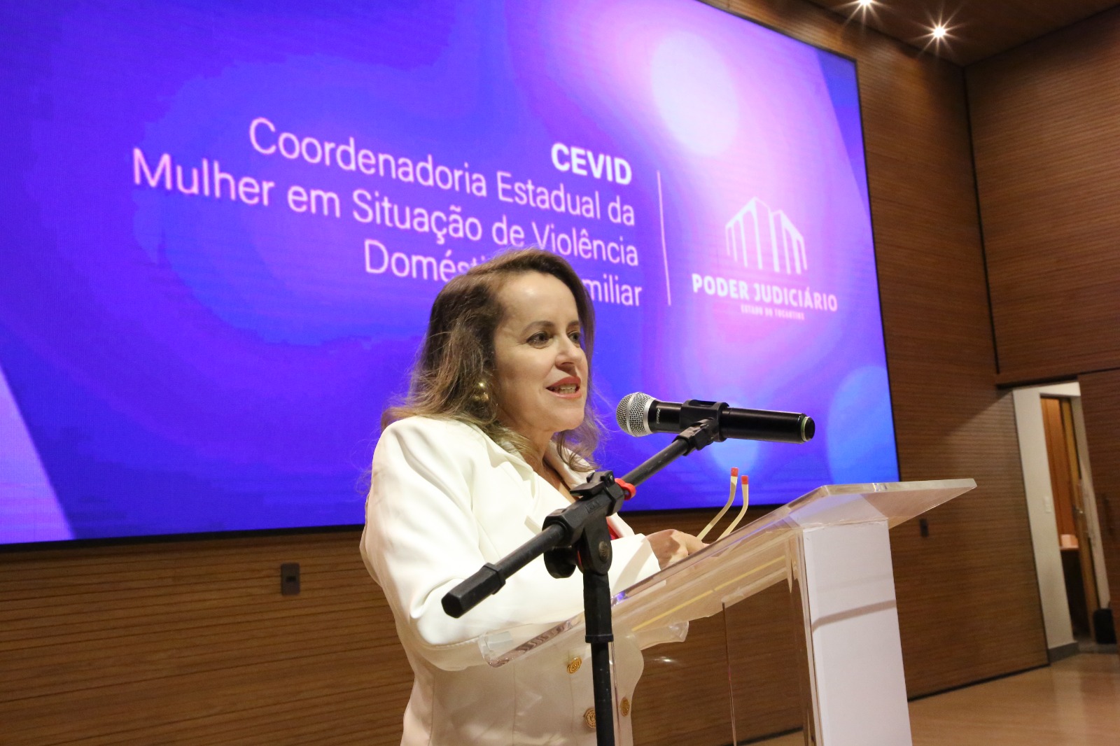 Fotografia de mulher branca fala ao microfone 
