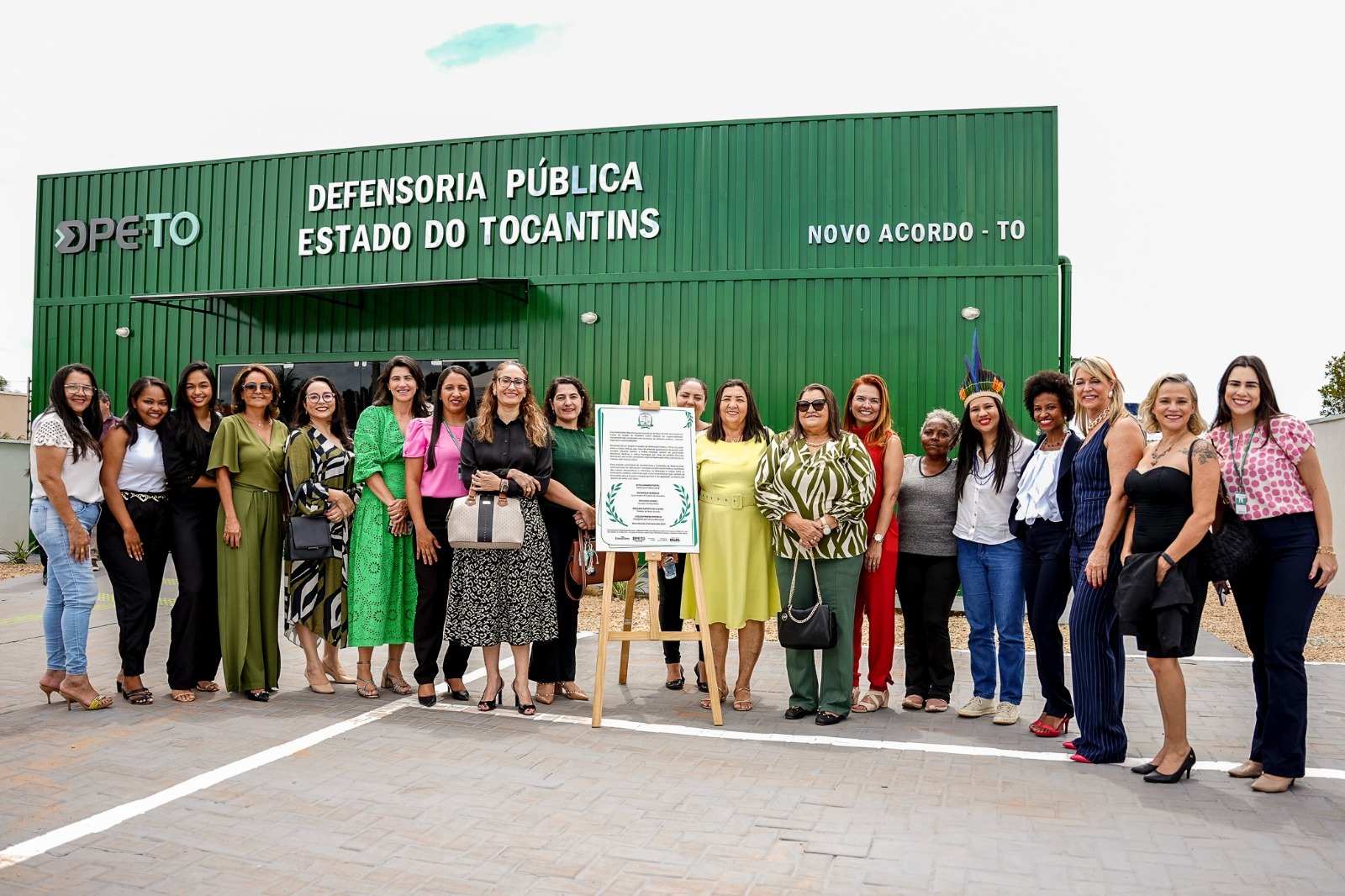 Homens e mulheres em pé em frente a uma obra sustentável inaugurada pela Defensoria Pública usando contêiner pintado na cor verde