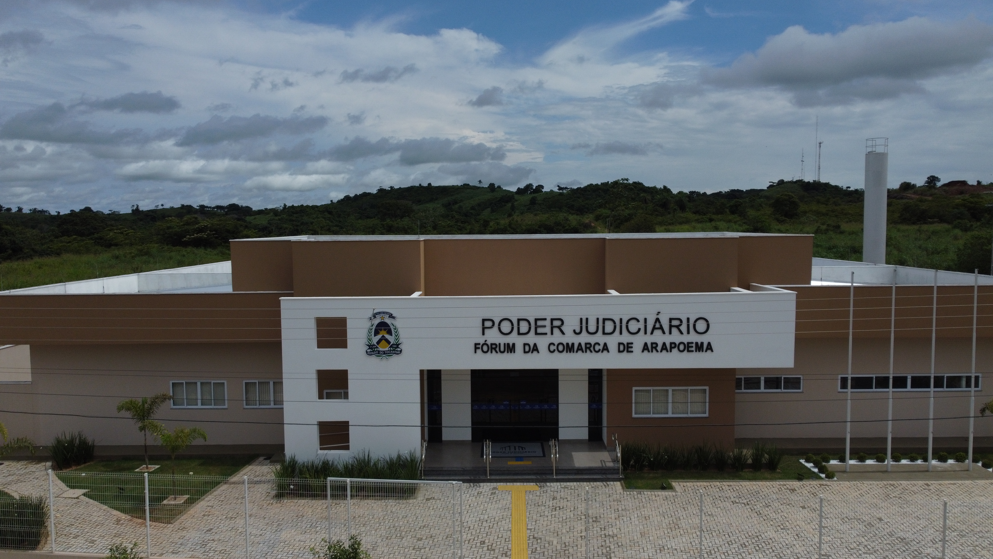 fachada do prédio do novo fórum de Arapoema; pintado nas cores marrom, bege e branco, janelas e portas de vidro; à frente o síbolo do Poder Judiciário e o nome Dórum da Comarca de Arapoema