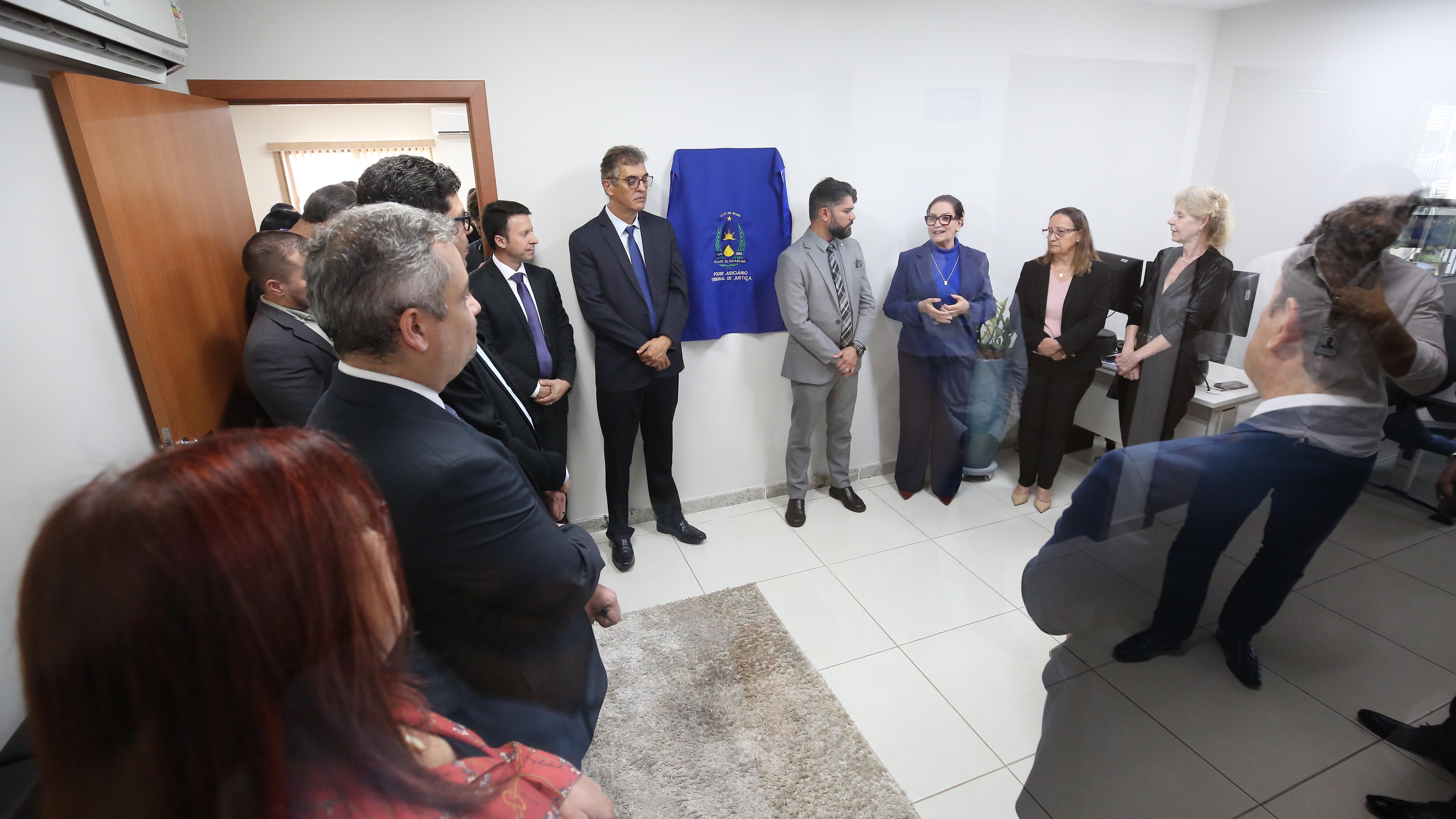 grupo de pessoas perfiladas escutam o pronunciamento de uma mulher enquanto aguardam o descerramento de uma placa coberta por um tecido azul