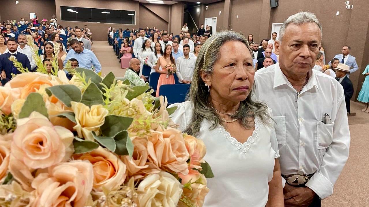 arranjo de flores ao lado de uma casal heterossexual, o homem e a mulher vestem roupas brancas