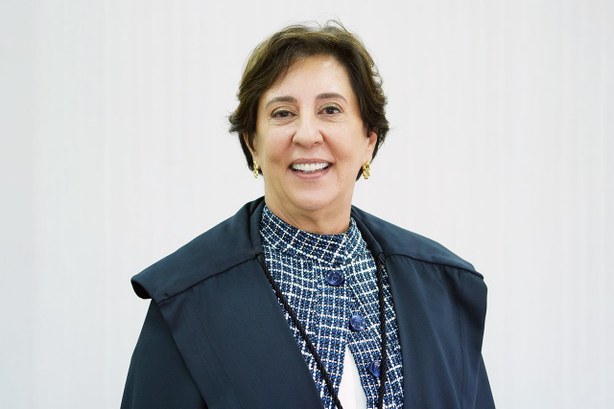 Fotografia colorida da desembargadora Ângela Issa Haonat de cabelo solto curto, sorrindo, de toga e roupa xadrez azul por dentro 