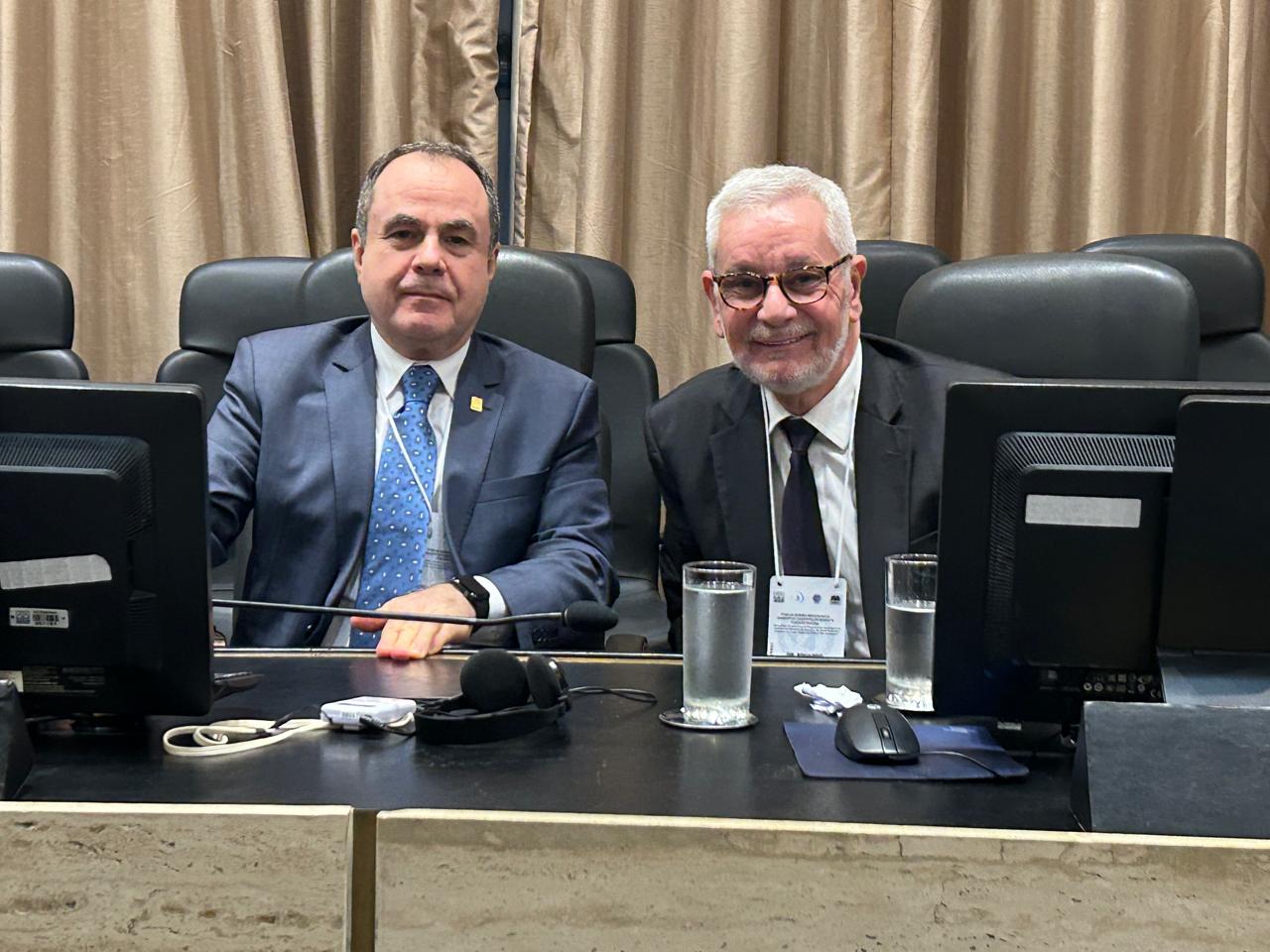 Imagem colorida que mostram dois homens sentados à  mesa em evento