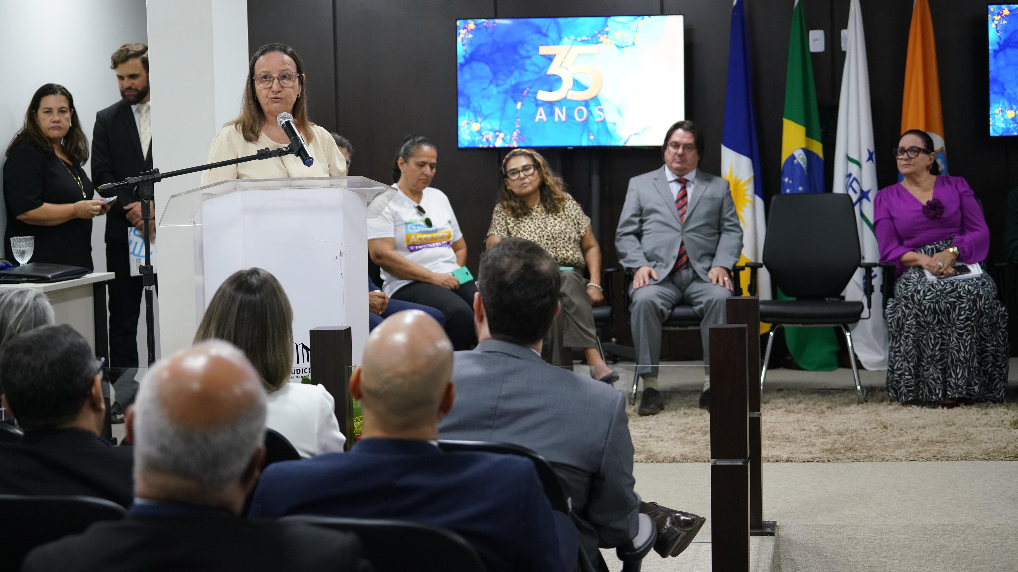 Fotografia colorida que mostra uma mulher branca e de óculos usando um púlpito 