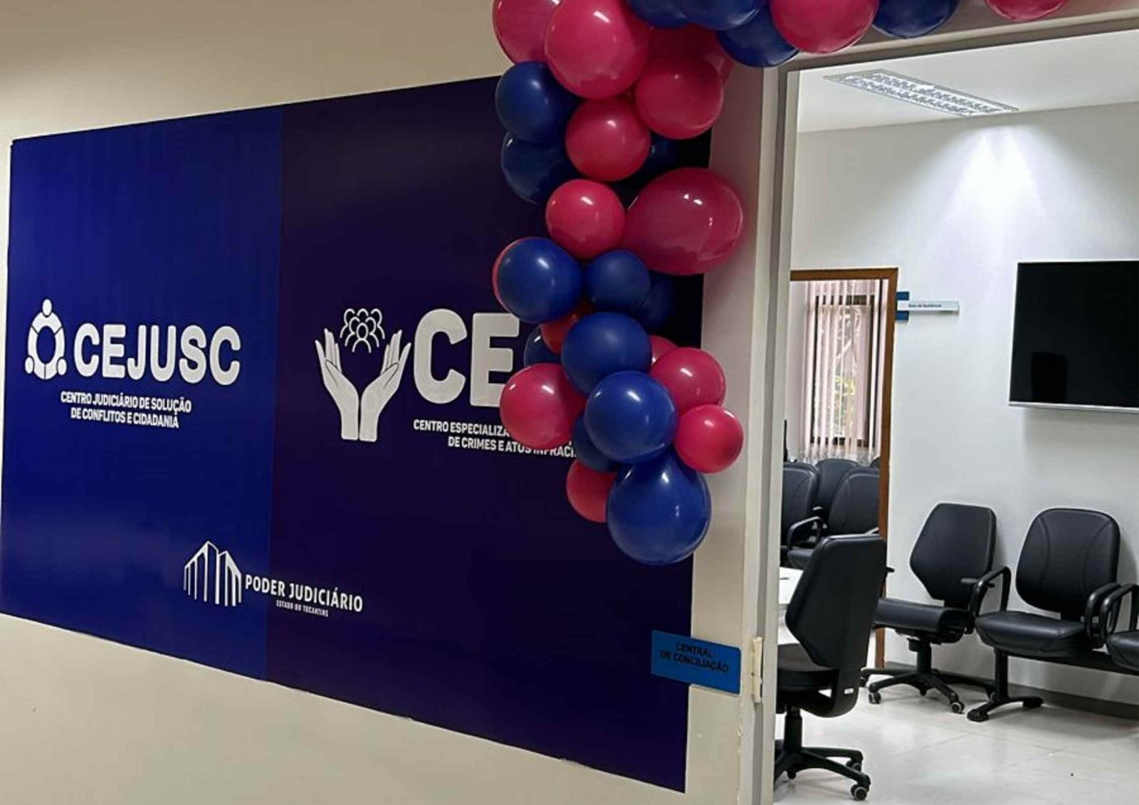 Imagem colorida que mostra a porta de uma sala com nome Cejusc em fundo azul e balões coloridos azuis e rosa