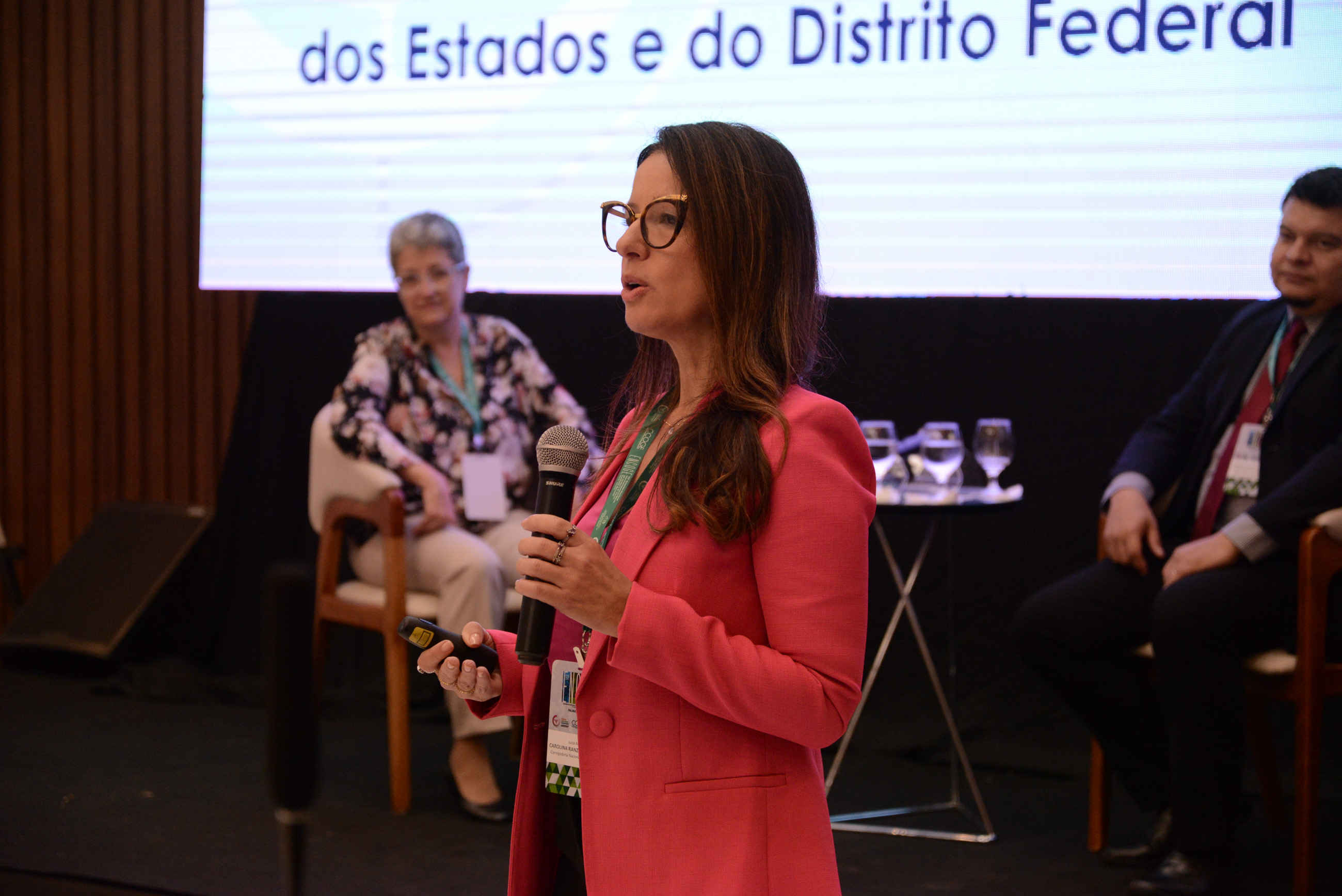 Fotografia colorida de uma mulher branca, usando rosa, palestrando no Fórum Nacional 
