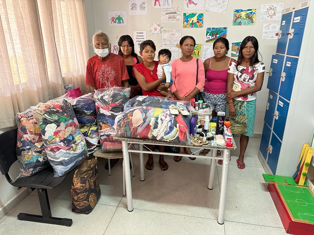 6 indígenas adultos em pé, uma jovem com uma criança indígena no colo; à frente os kits de objetos doados por servidores da comarca de Araguaína