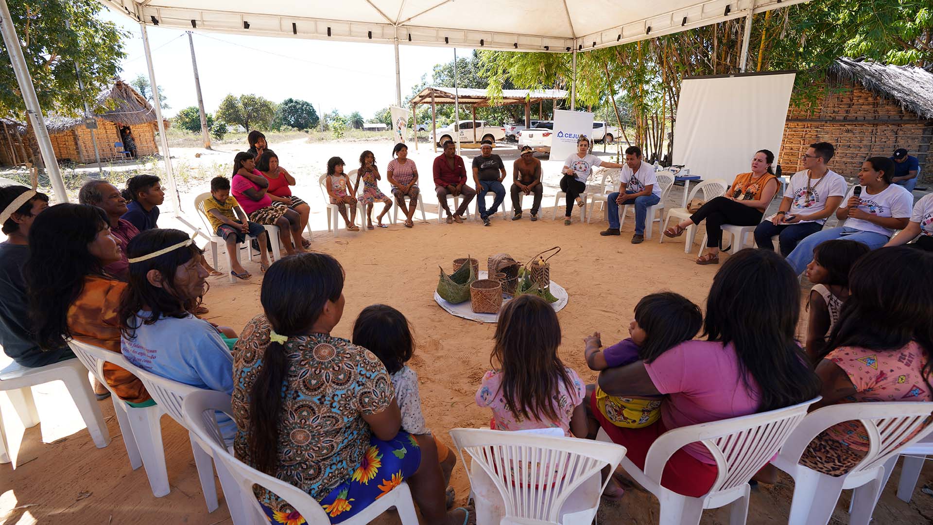 indígenas, magistrada e servidores do Judiciário reunidos em circulos, sentados em cadeiras brancas para dinâmica do círculos restaurativos de construção de paz, ao centro os elementos da Justiça Restaurativa