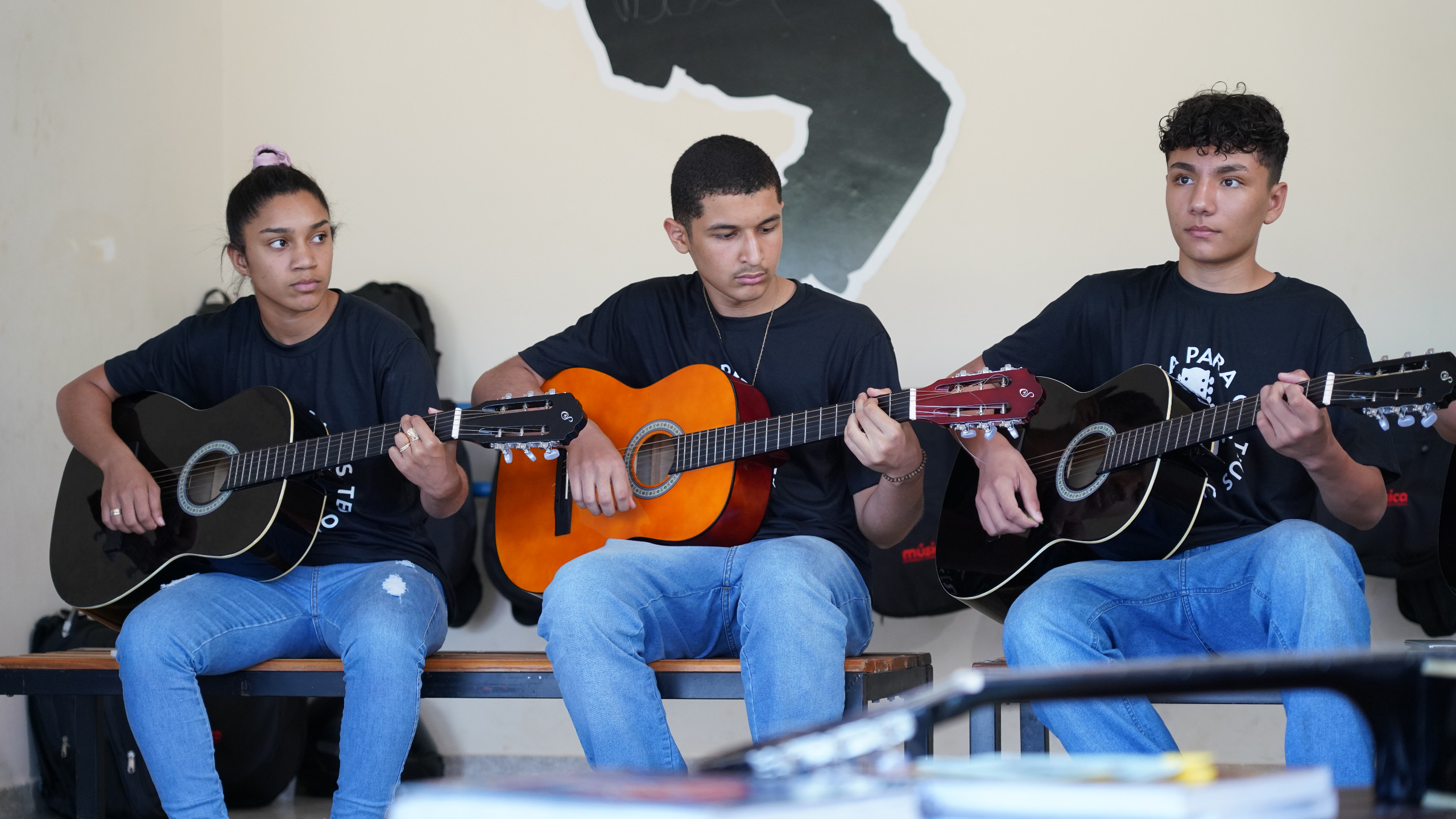 Imagem mostra pessoas vestidas de calça e blusa preta segurando violões