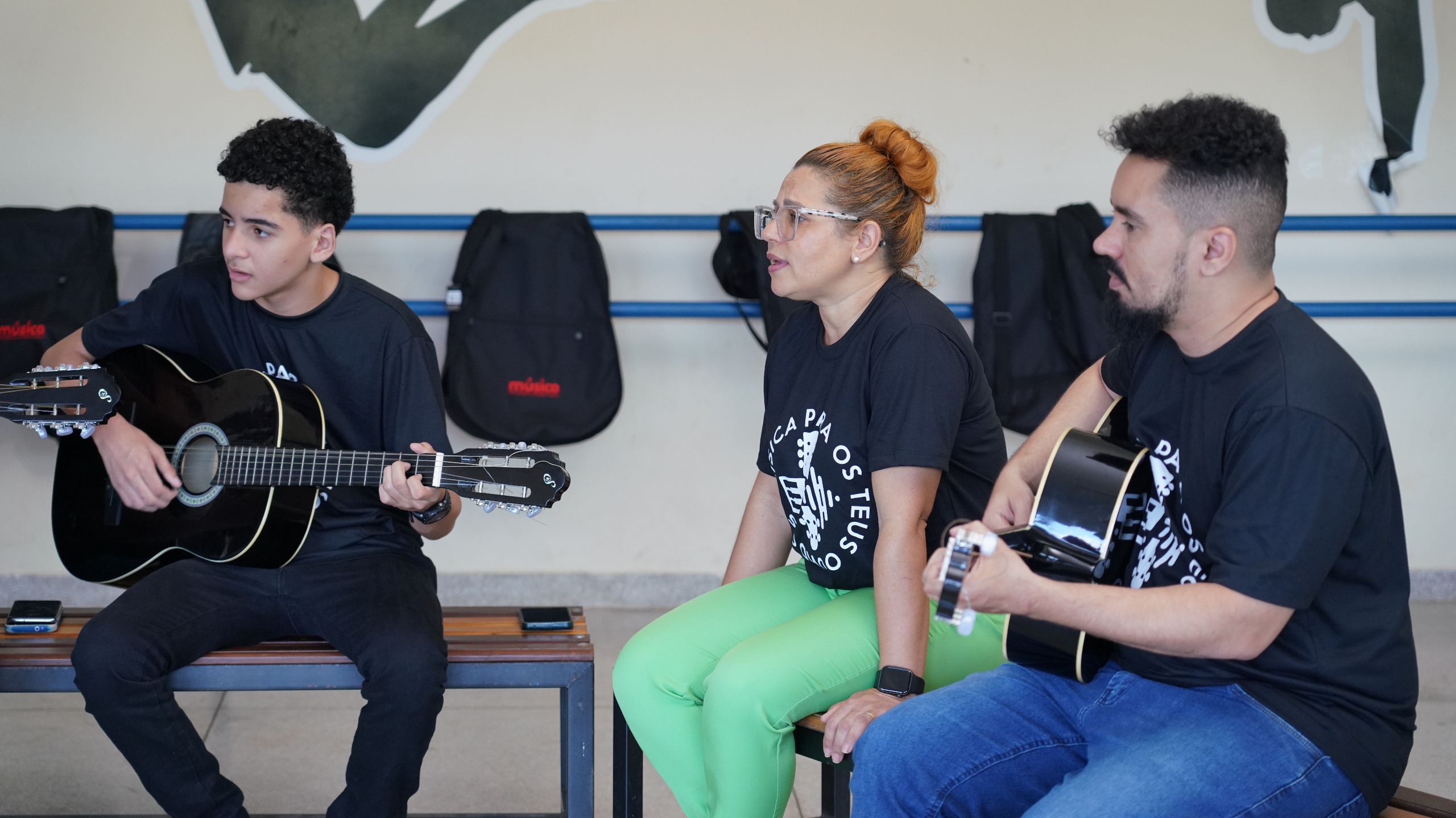 Imagem mostra pessoas vestidas de calça e blusa preta segurando violões
