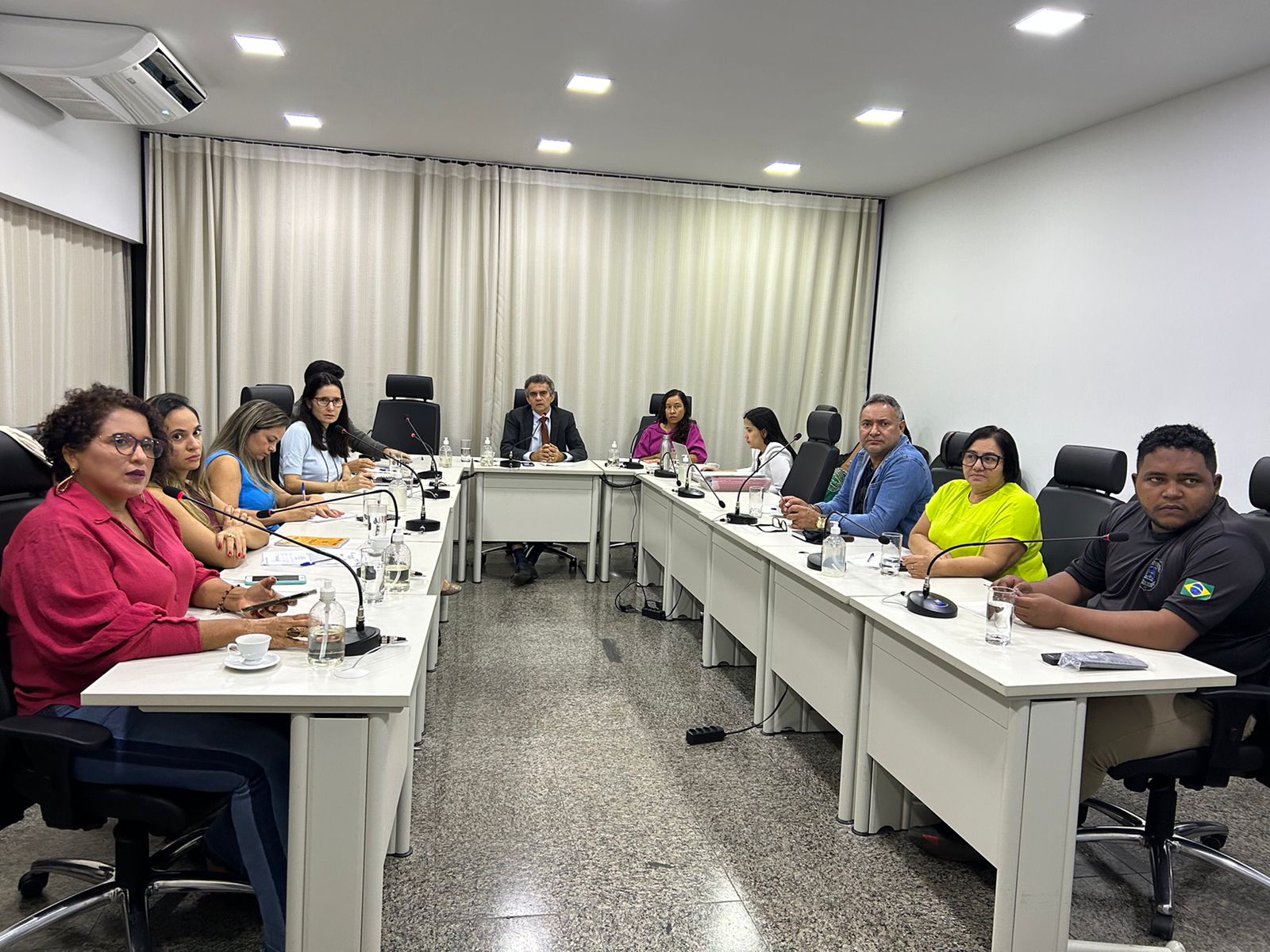 Homens e mulheres sentados em torno de mesa branca em formato de U