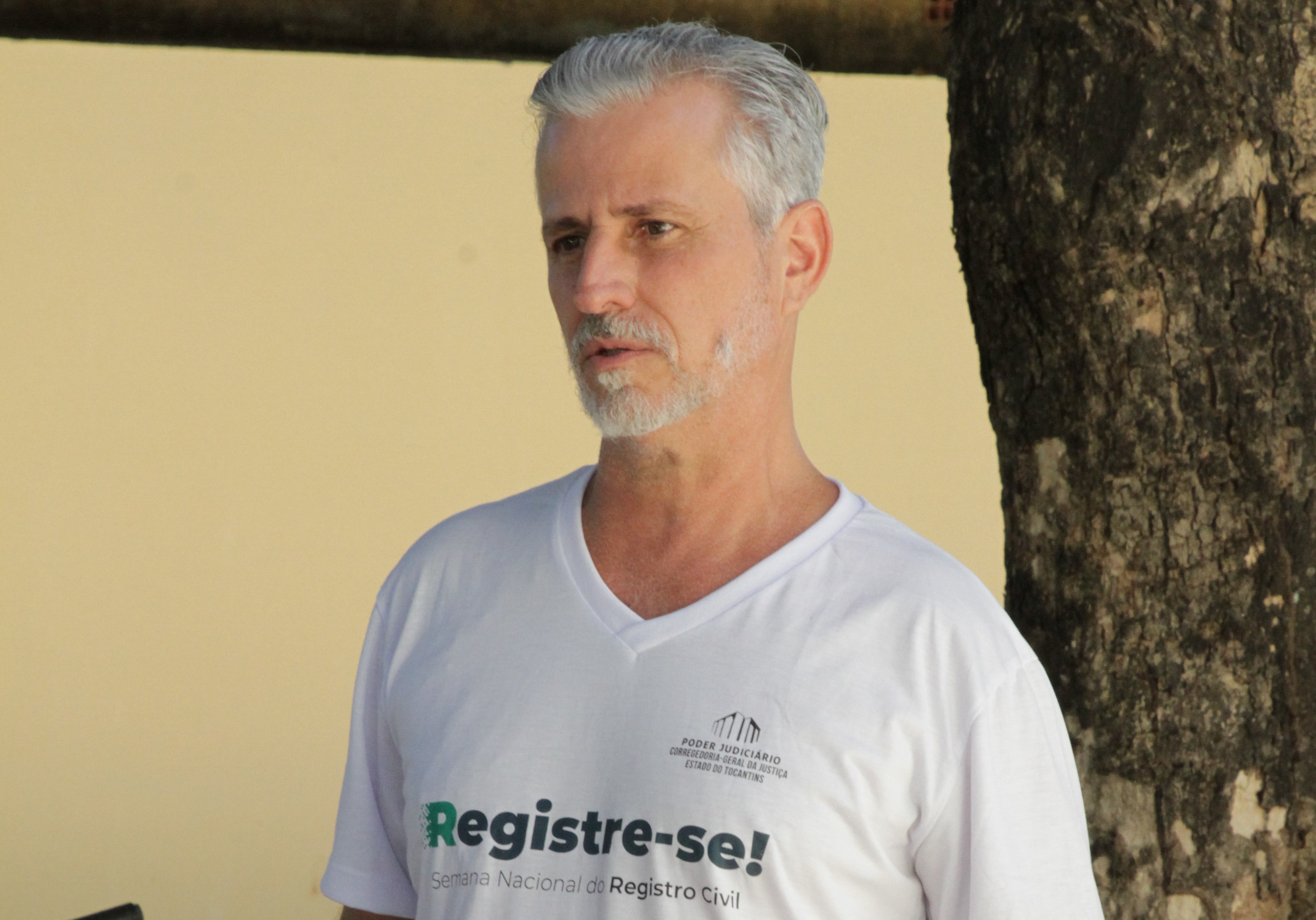 Juiz Esmar, um home de cabelos grisalhos e barba, com uma camiseta branca do Registre-se 