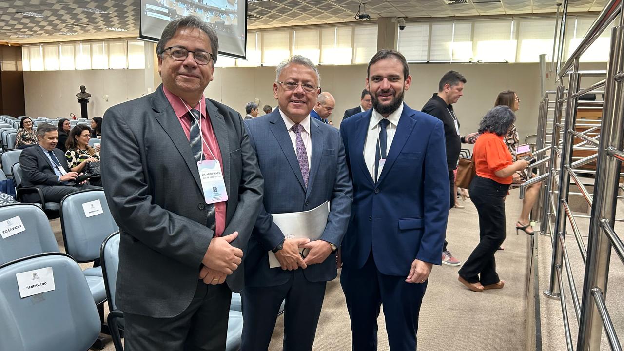Em pé, de frente os juízes Arióstenis Guimarães (de óculo e terno cinza, camisa vermelha, gravata cinza e branca, e crachá); o presidente do Fonamec ao centro (cabelos bancos, de óculos, usa terno azul acinzentado, camisa branca e gravata em tons de lilás); e o juiz José Carlos à direita (tem barba e usa terno e gravata azul e camisa branca) 
