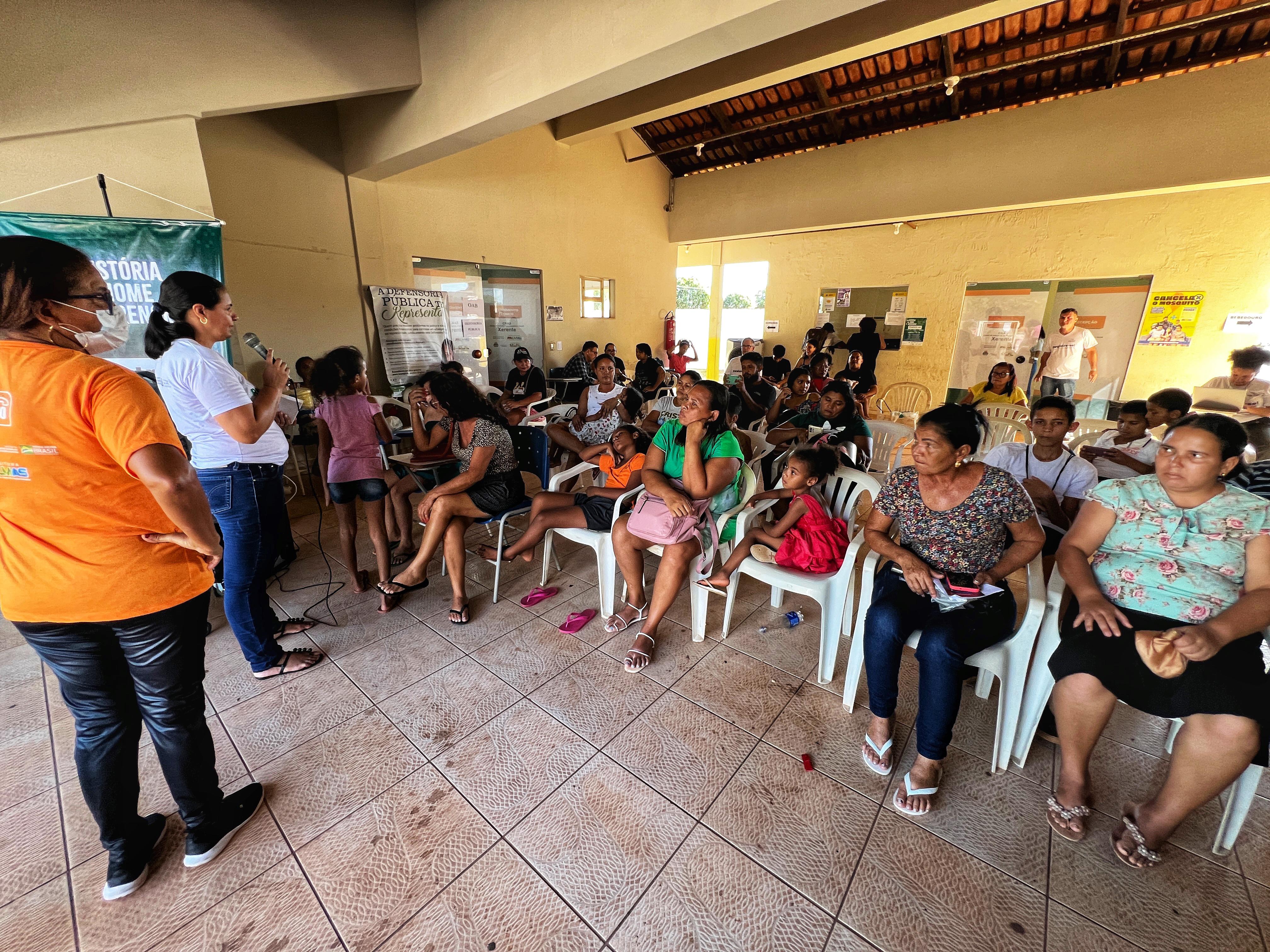Várias pessoas sentadas em cadeiras ouvindo a equipe do Registre-se falando ao microfone