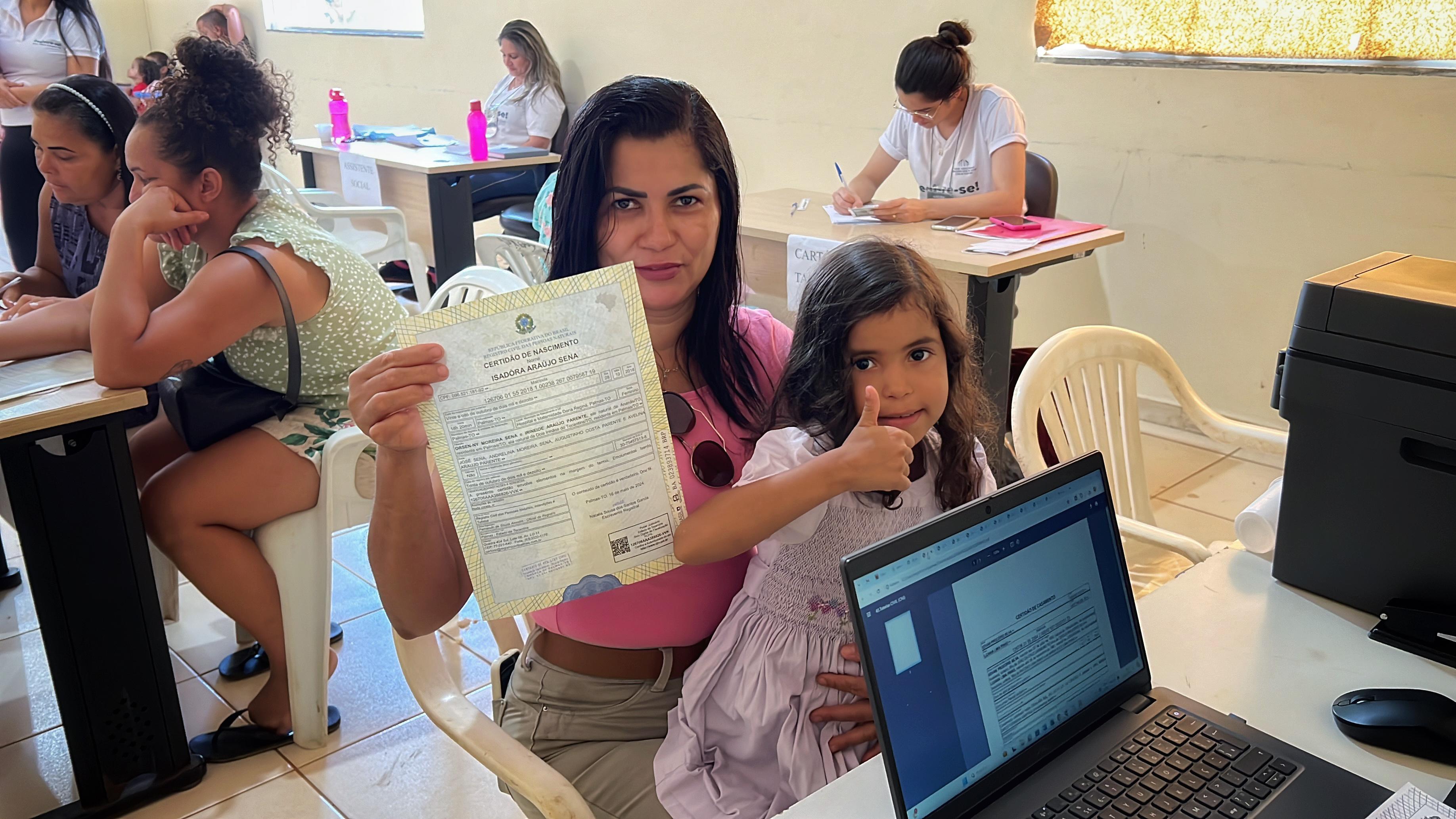 Mulher com uma criaça no colo segurado a certidão de nascimento da filha