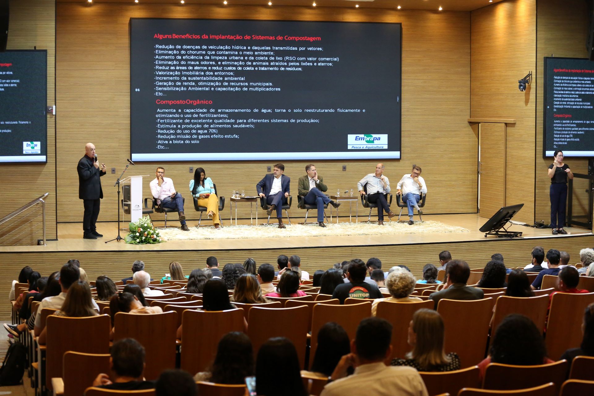 Homem calvo, de terno preto fala ao público em um auditório