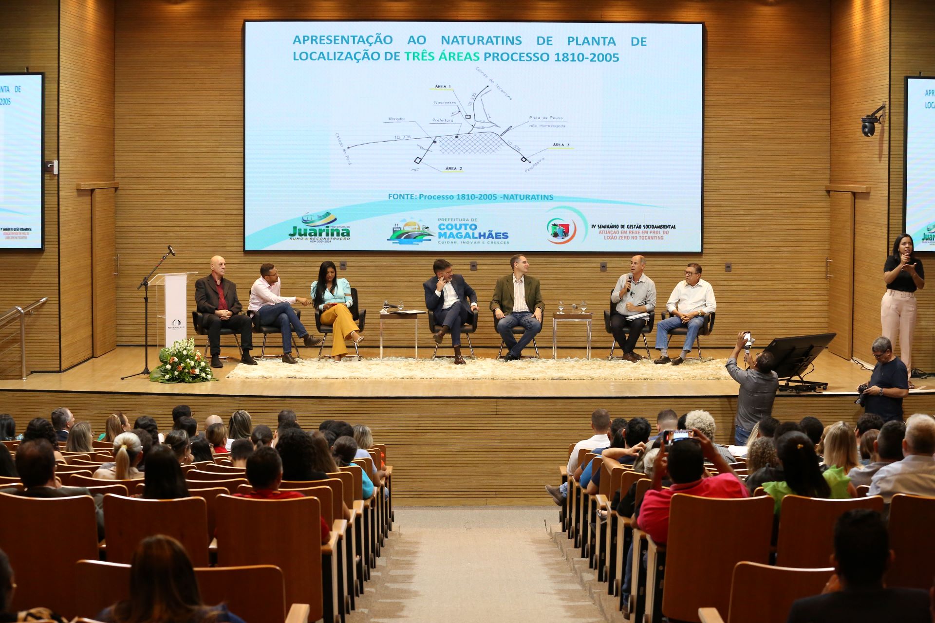 Homem branco sentado ao lado de outras pessoas está em cima do palco e fala em um microfone