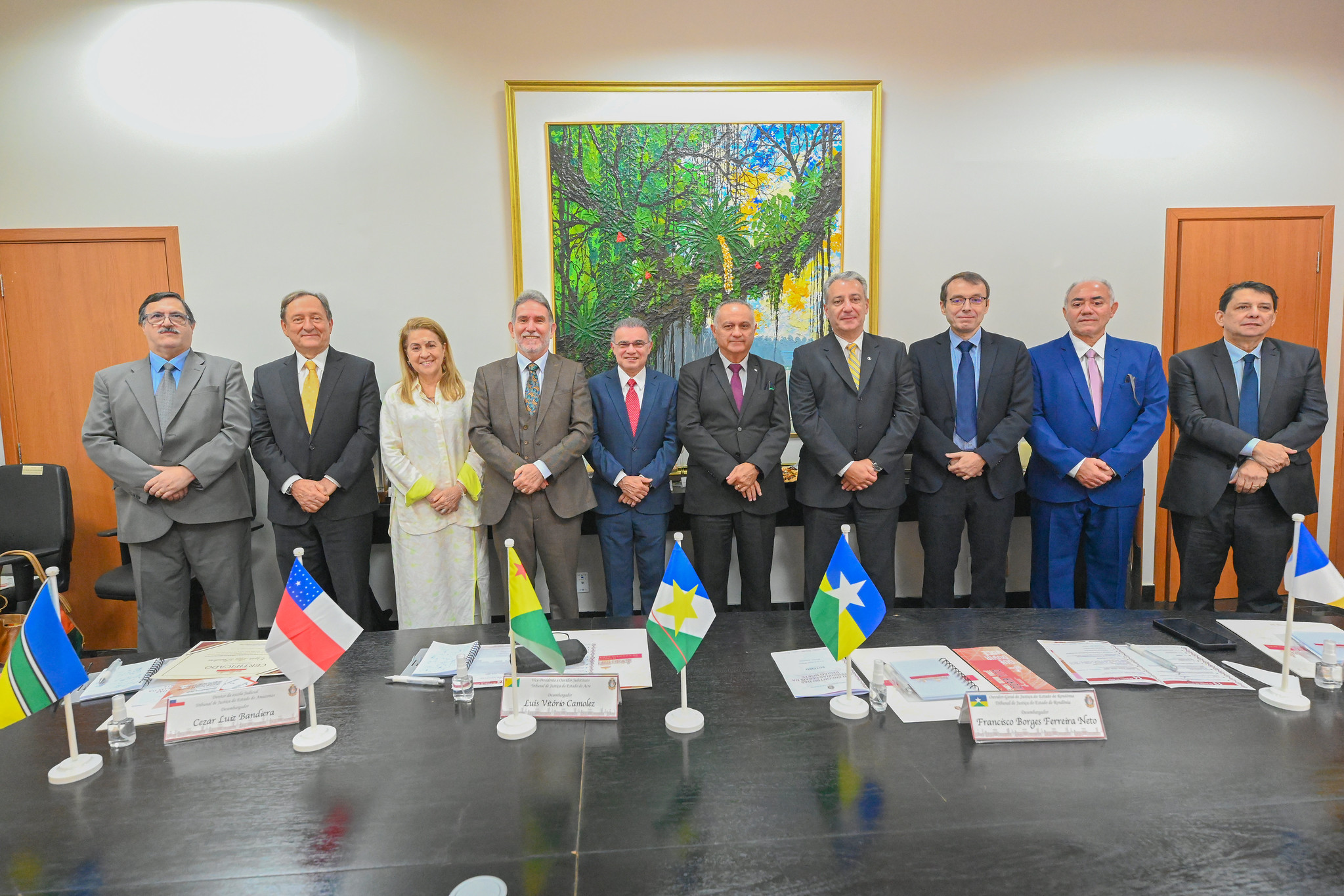 Imagem colorida que mostra homens e mulheres bem trajados, em pé, posando para a foto. À frente deles, têm bandeiras dos estados à frente