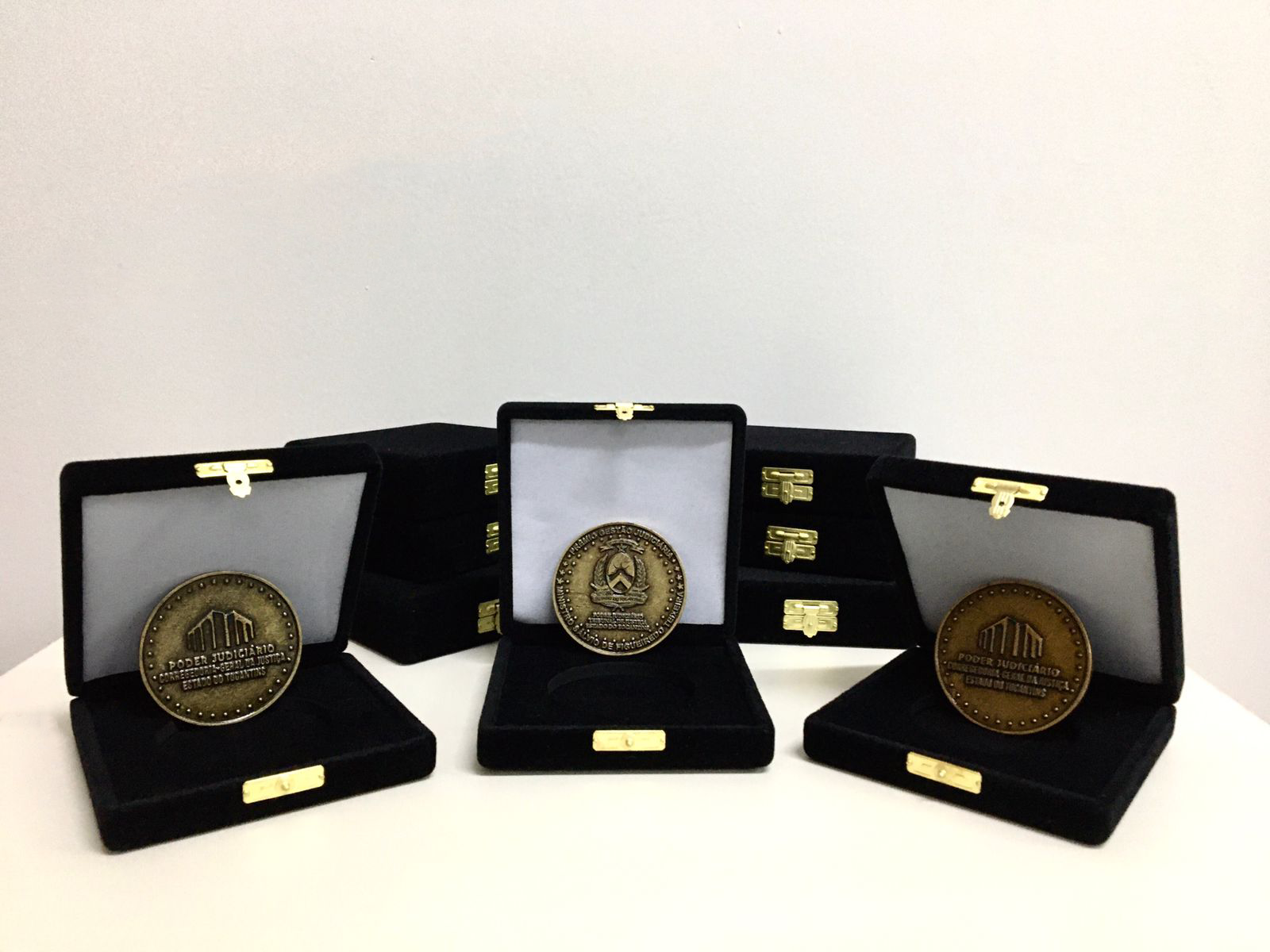 Imagem colorida que mostra três caixas pretas com três medalhas em bronze dentro