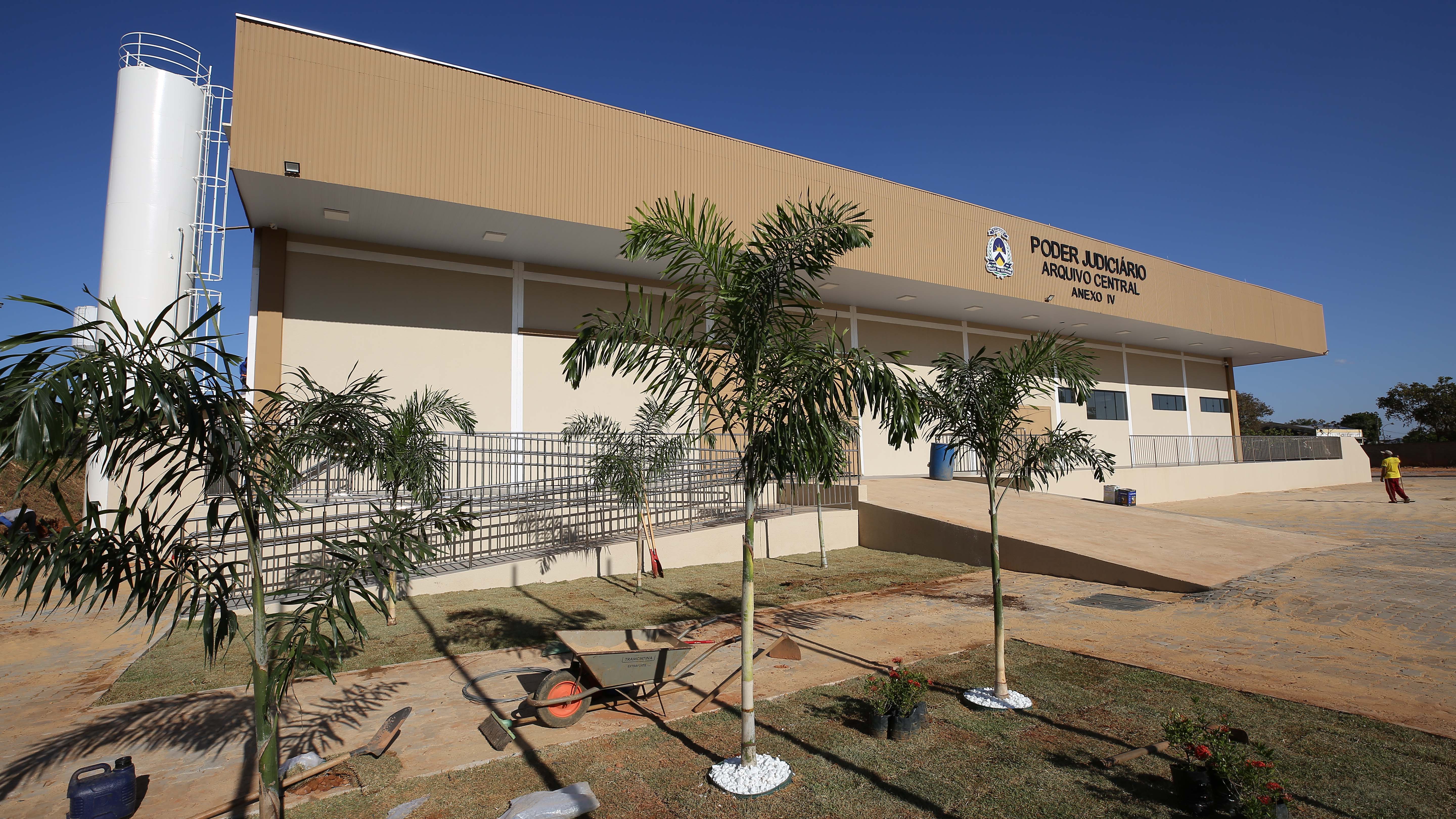 Imagem mostra um prédio nas cores marrom em frente paisagismo com coqueiros