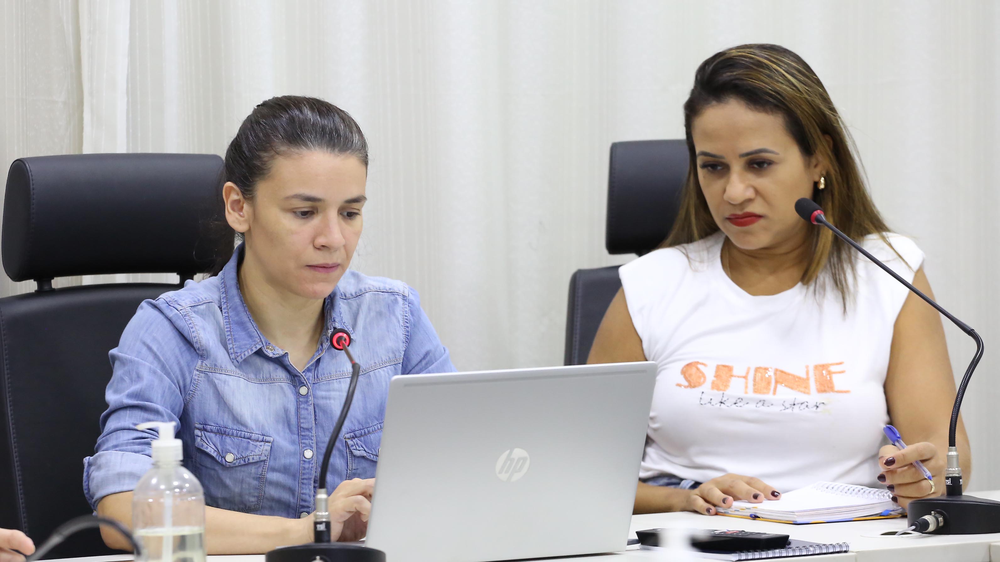 duas mulheres estão sentadas olhando para um notebook que está sobre a mesa