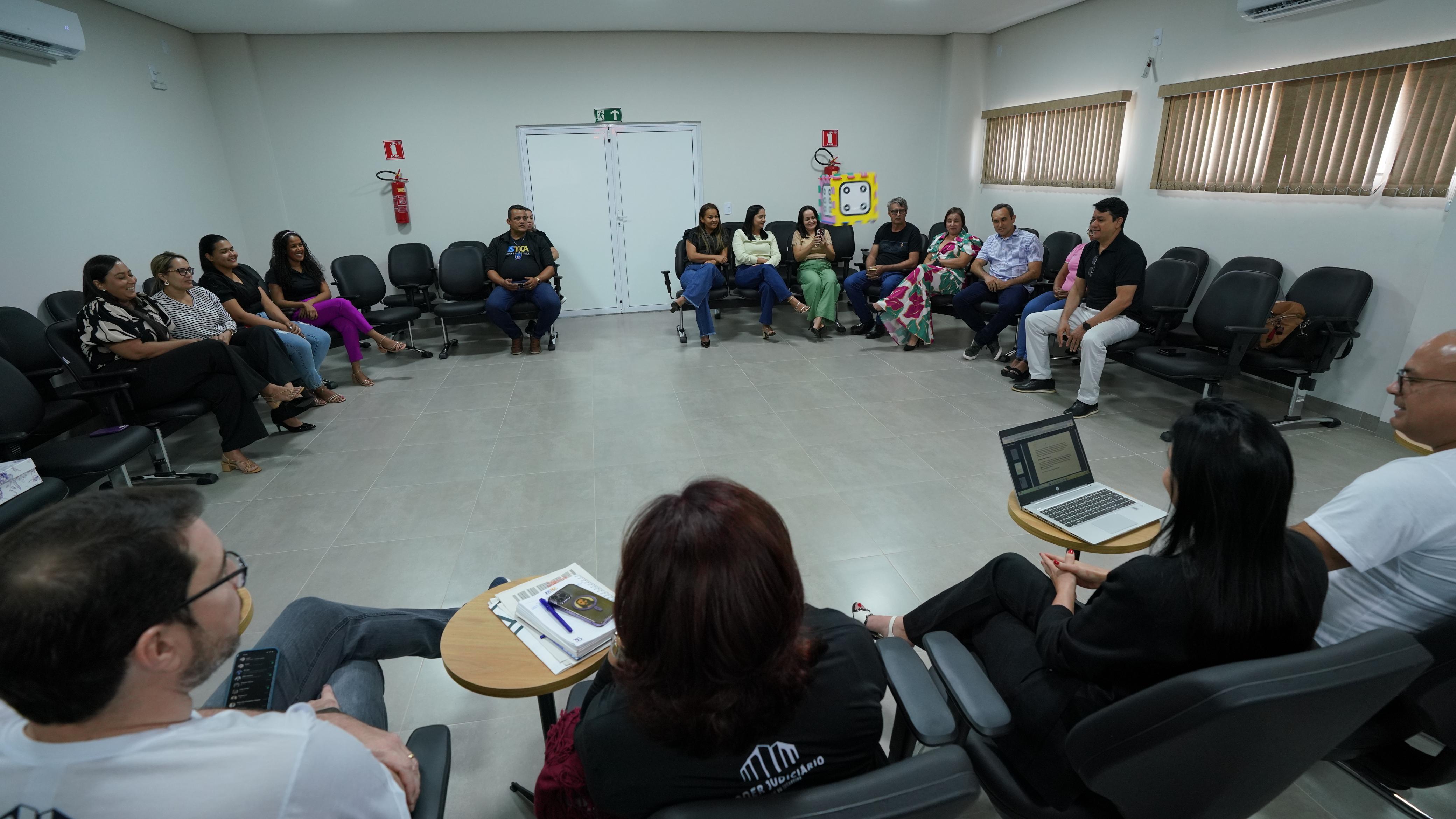 Fotografia colorida que mostra pessoas reunidas em uma sala, em formato de roda. Todas estão sentadas