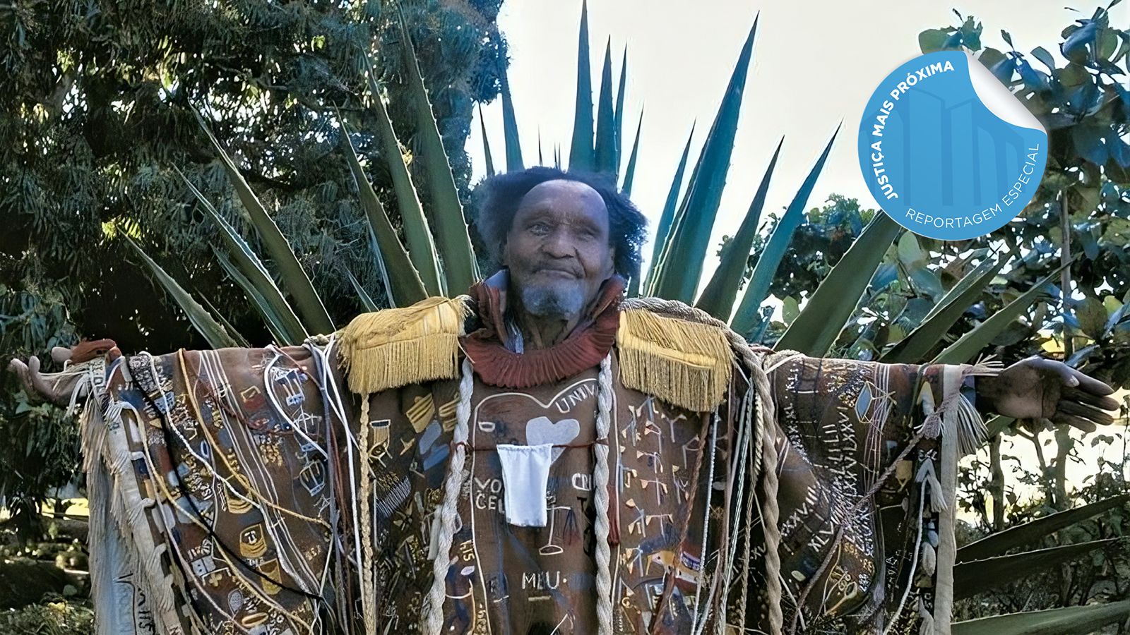 homem negro posa para foto de braços abertos ele veste uma túnica semelhante a de um rei