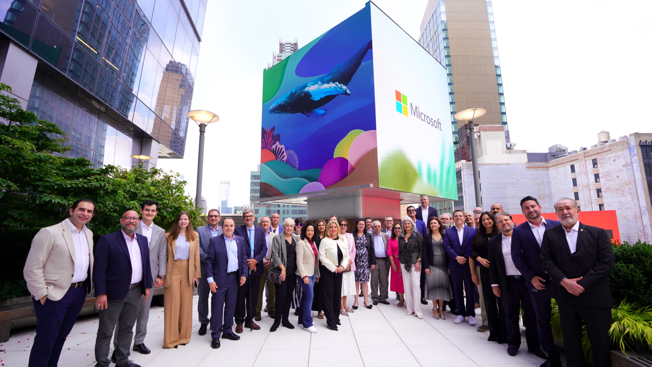 Membros do Colégio Permanente dos Diretores das Escolas Estaduais da Magistratura reunidos na frente de um prédio; Na fachada um grande painel com uma imagem colorida do fundo do mar e um peixe grande; à direita a logo e a palavra Microsoft