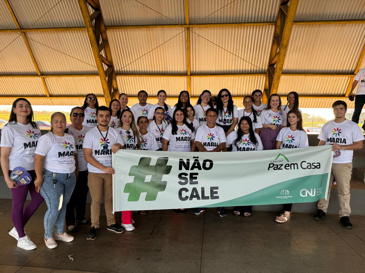 Equipe do Judiciário, com camisetas do Maria nas Comunidades, em pé, com a faixa da Semana da Justiça pela Paz em Casa, concentrados para a caminhada do Agosto Lilás