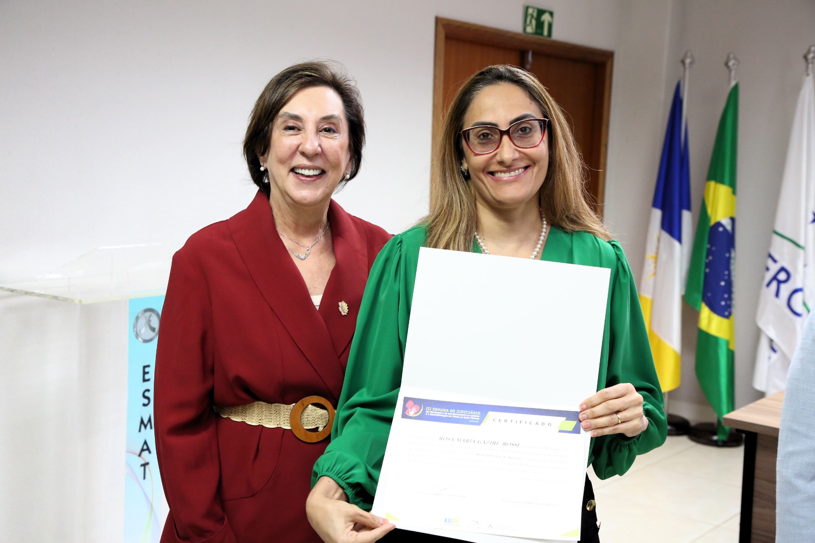 Fotografia colorida de duas mulheres bem vestidas segurando um certificado
