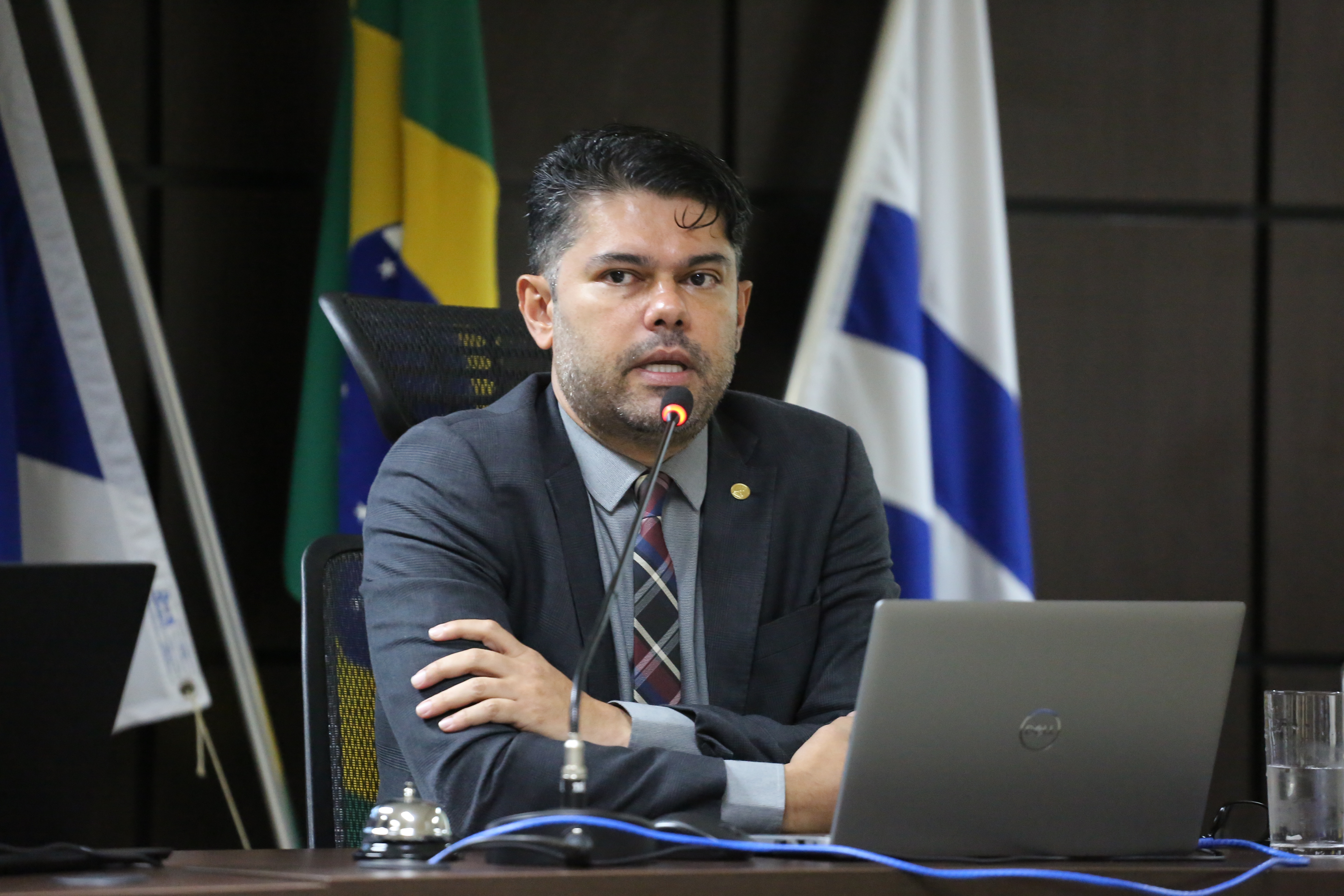magistrado sentado, de braços cruzados sobre uma mesa fala ao microfone. ele usa terno cinza escuro, camisa cinza claro e gravata xadrez nas cores preto, branco, vinho e azul marinho