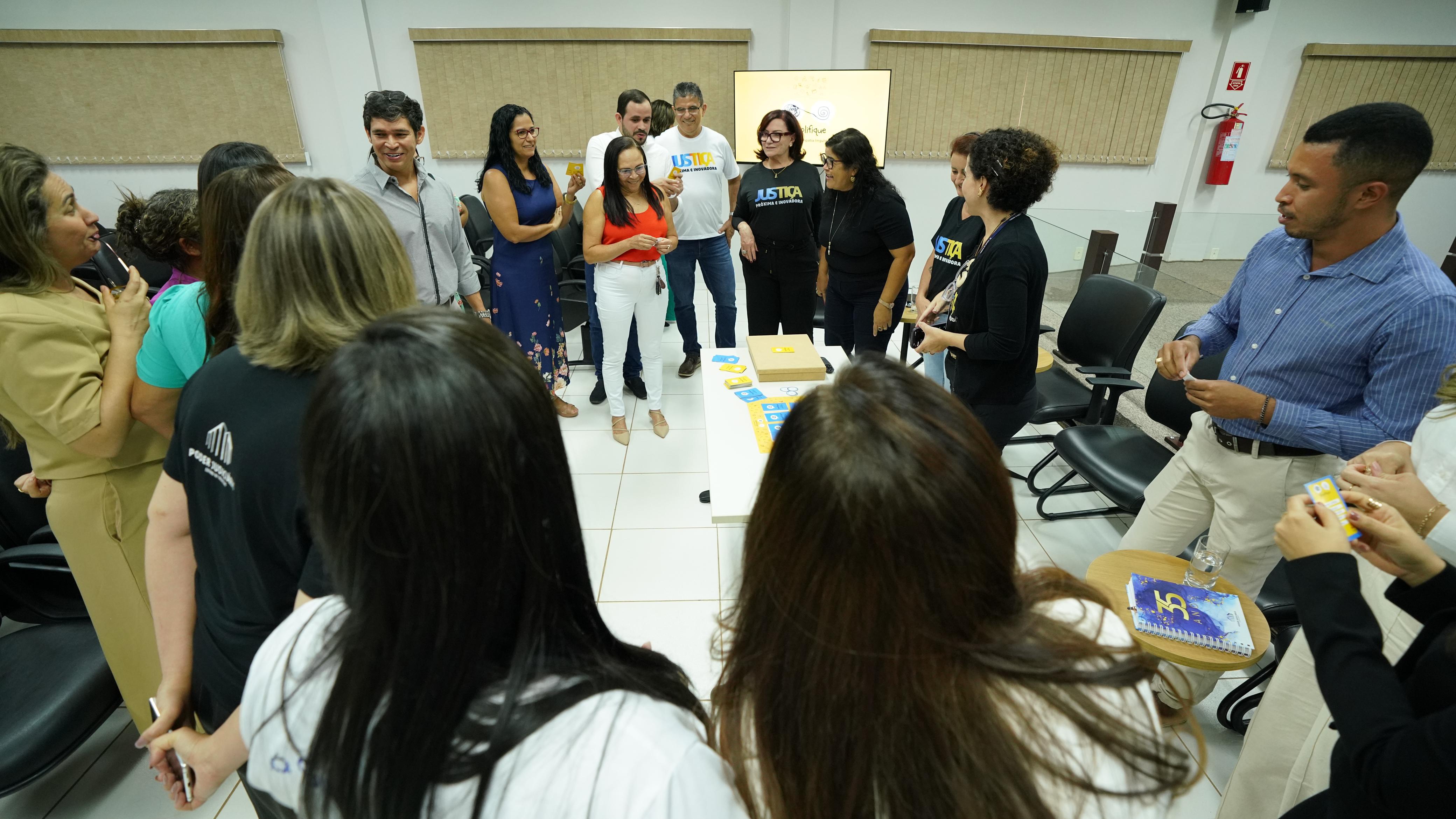 Homens e mulheres em pé formam toda de diálogo em sala de paredes brancas com persianas beges