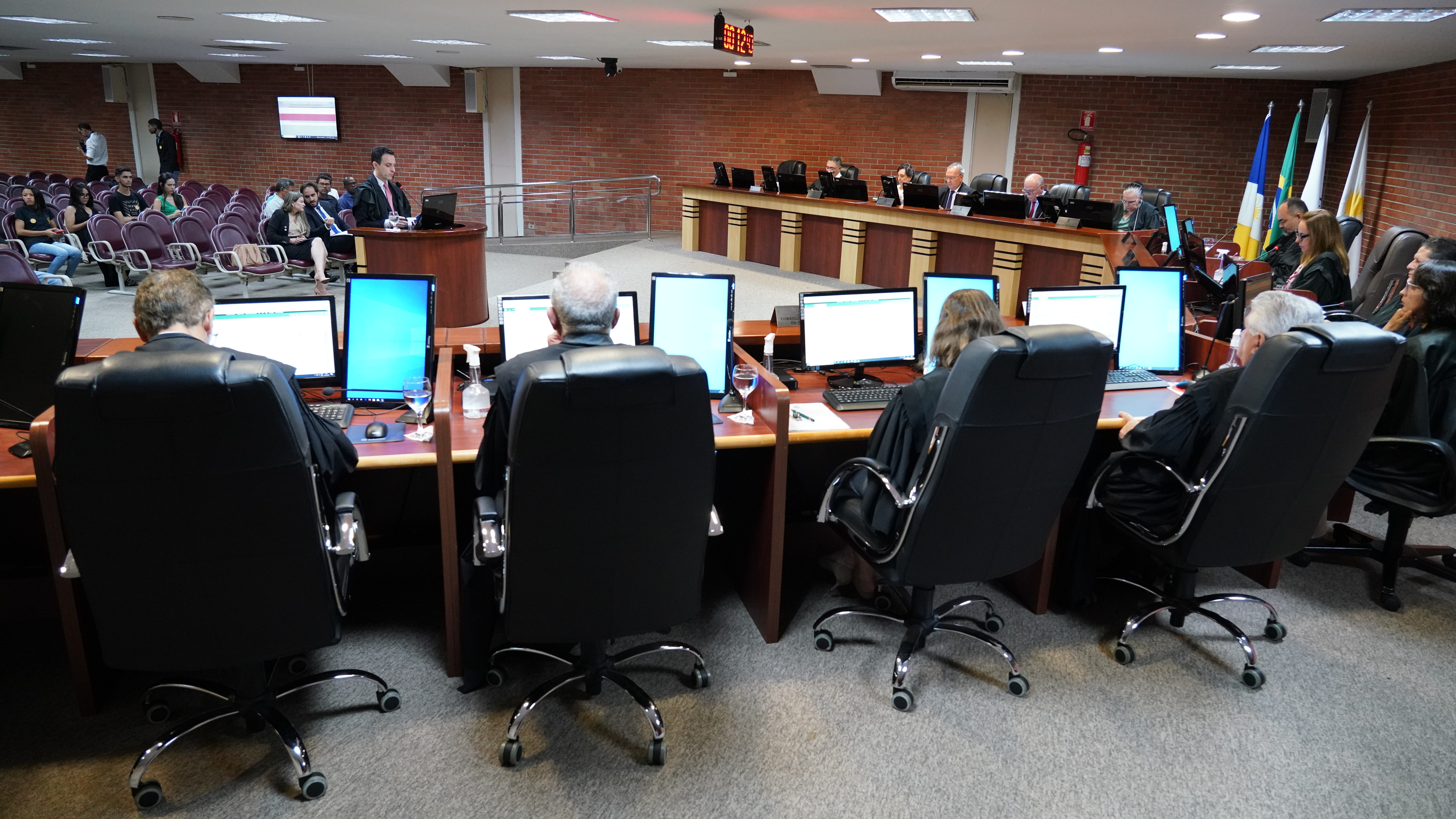 foto colorida horizontal mostra sessão no tribunal pleno do TJTO, em primeiro plano magistrados estão de costas sentados à bancada, obsevando ao centro da imagem advogado que realiza sustentação oral. Ao fundo, membros da sociedade civil assitem a sessão