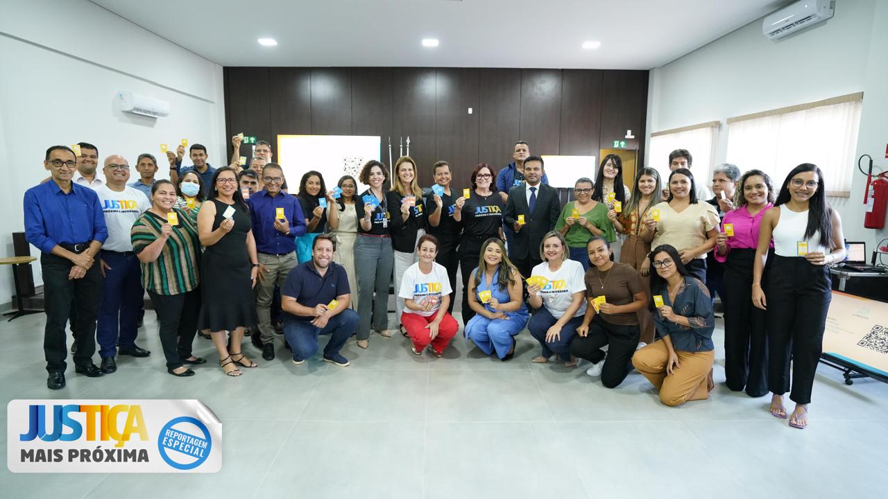 Homens e mulheres dentro de sala de paredes laterais brancas e parede de fundo de madeira escura. Eles posam para foto segurando um cartão amarelo