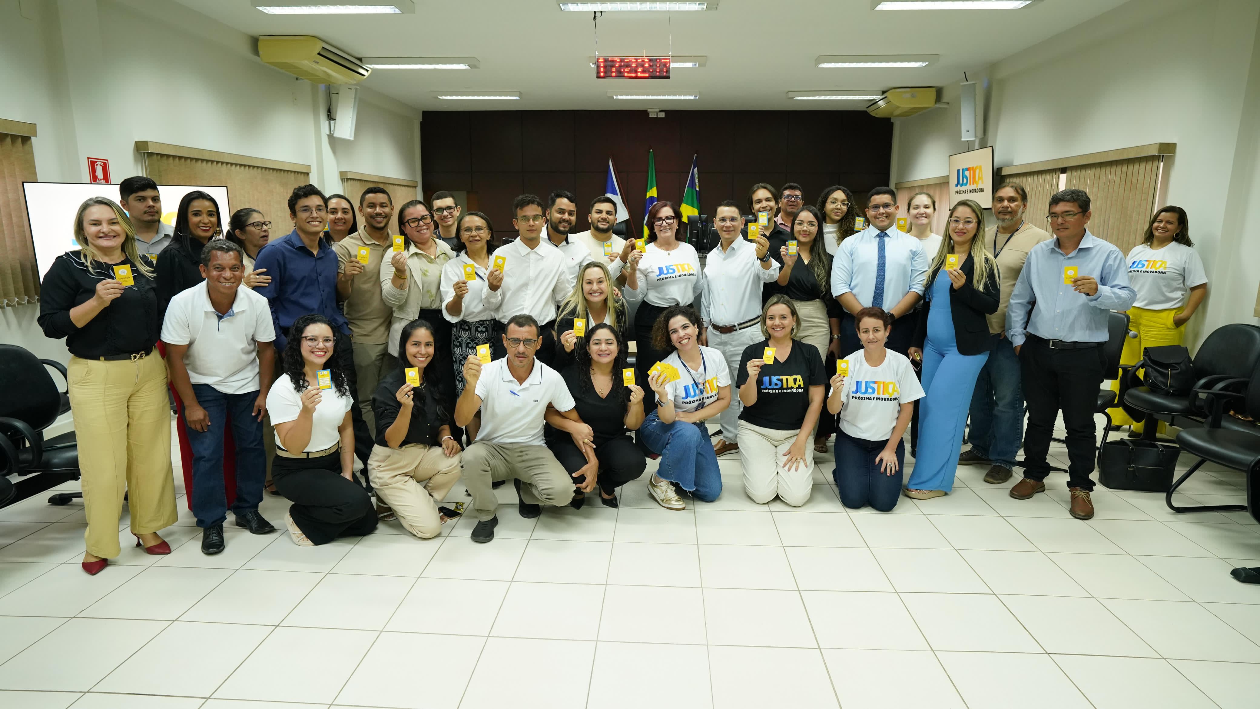 Imagem colorida que mostra dezenas de pessoas posando pra foto com um card na mão. As pessoas estão felizes