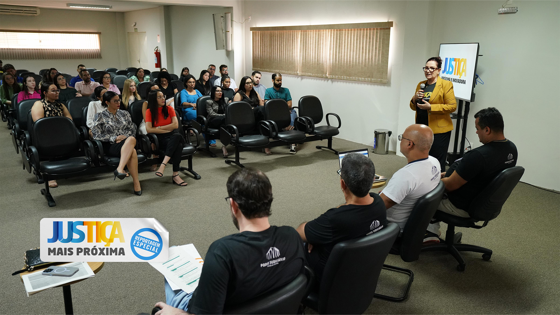 Fotografia colorida que mostra a presidente do TJTO usando mostarda e falando ao microfone para uma plateia atenta em um auditório.