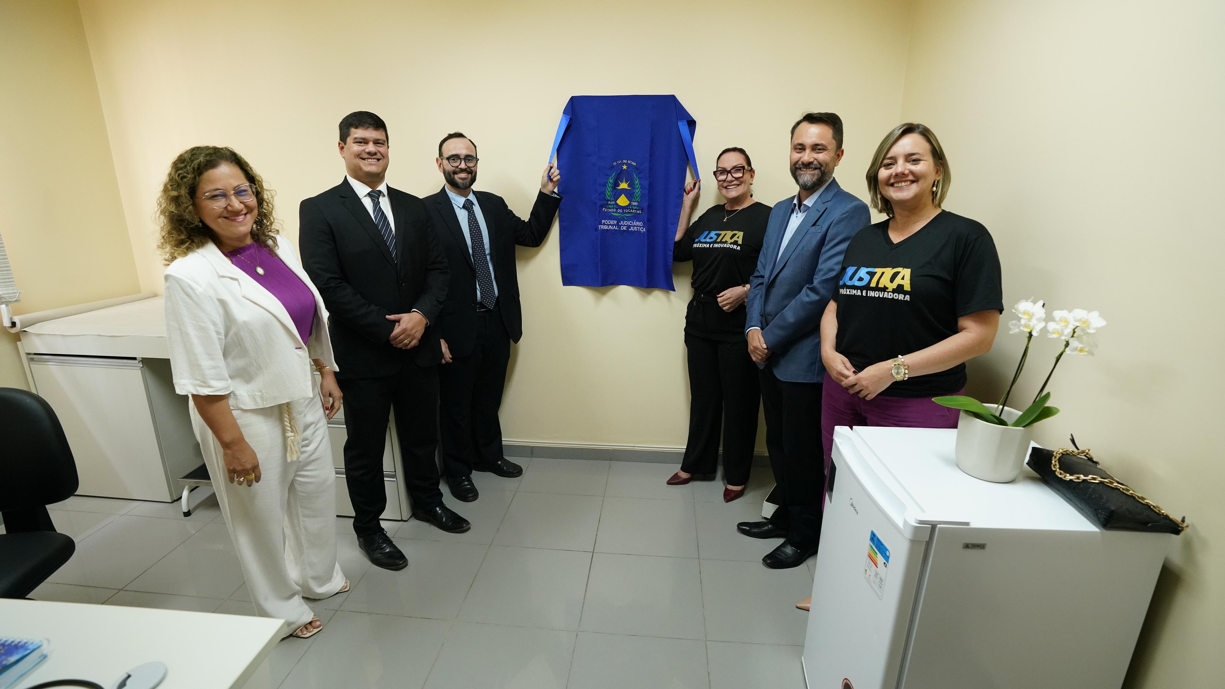 Fotografia colorida que mostra homens e mulheres segurando um tecido azul que cobre uma placa de inauguração da sala de perícias