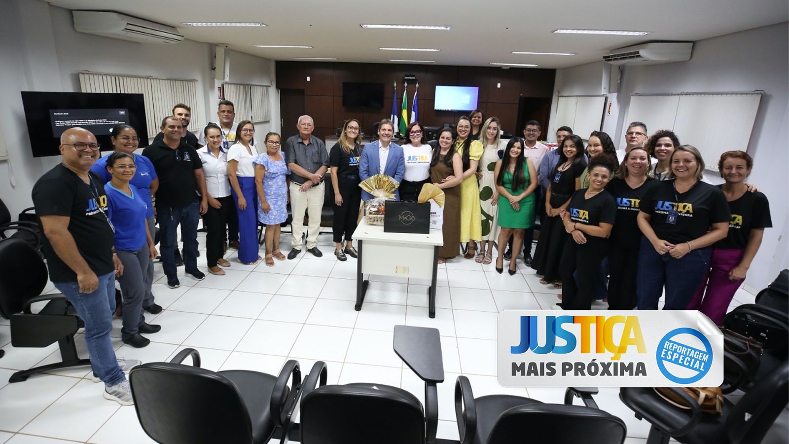 foto colorida horizontal mostra homens e mulhres de pé sorrindo no salão do juri do forum de goiatins