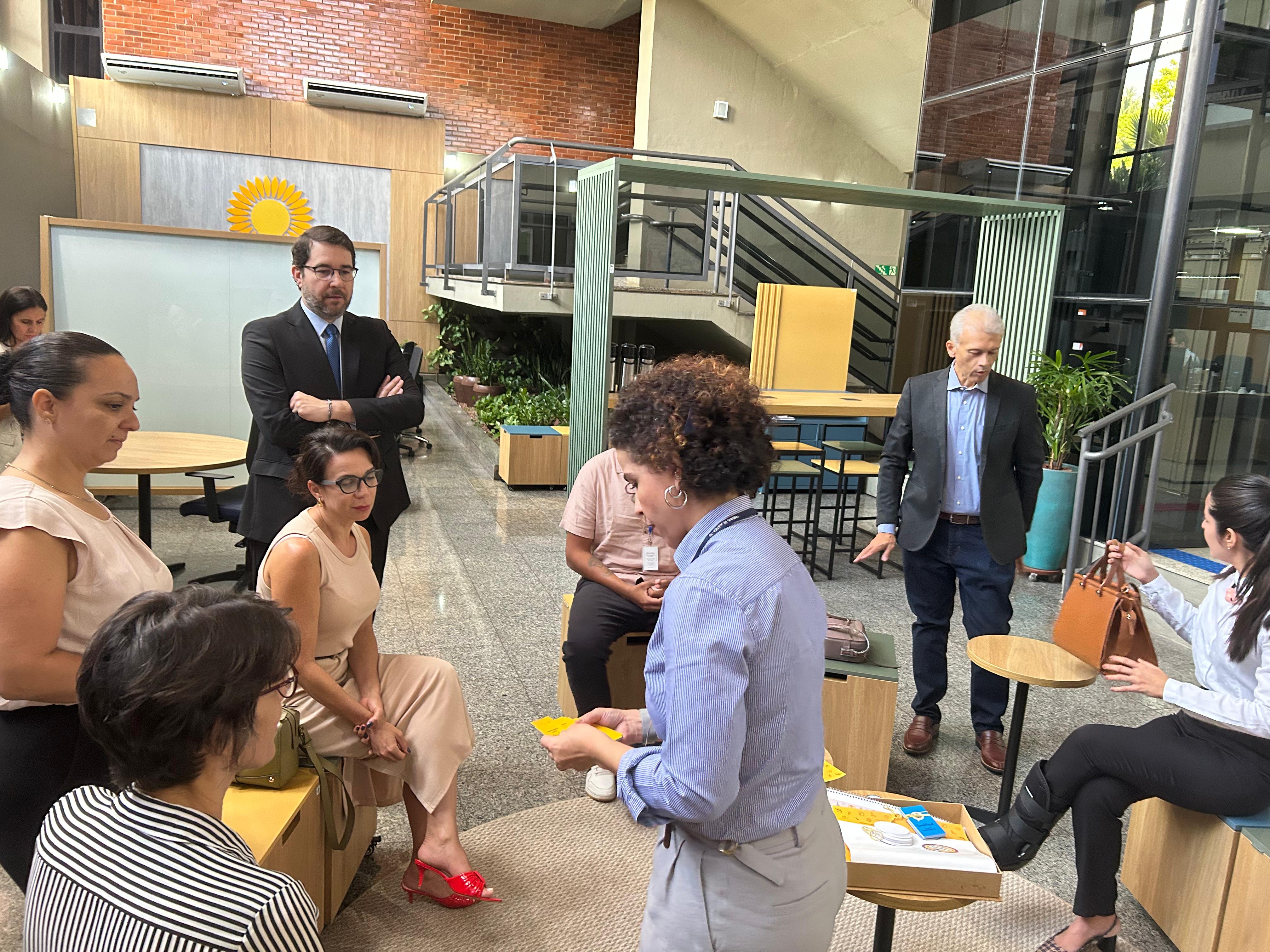 Foto mostra pessoas sentadas e outras em pé jogando um jogo de cartas 