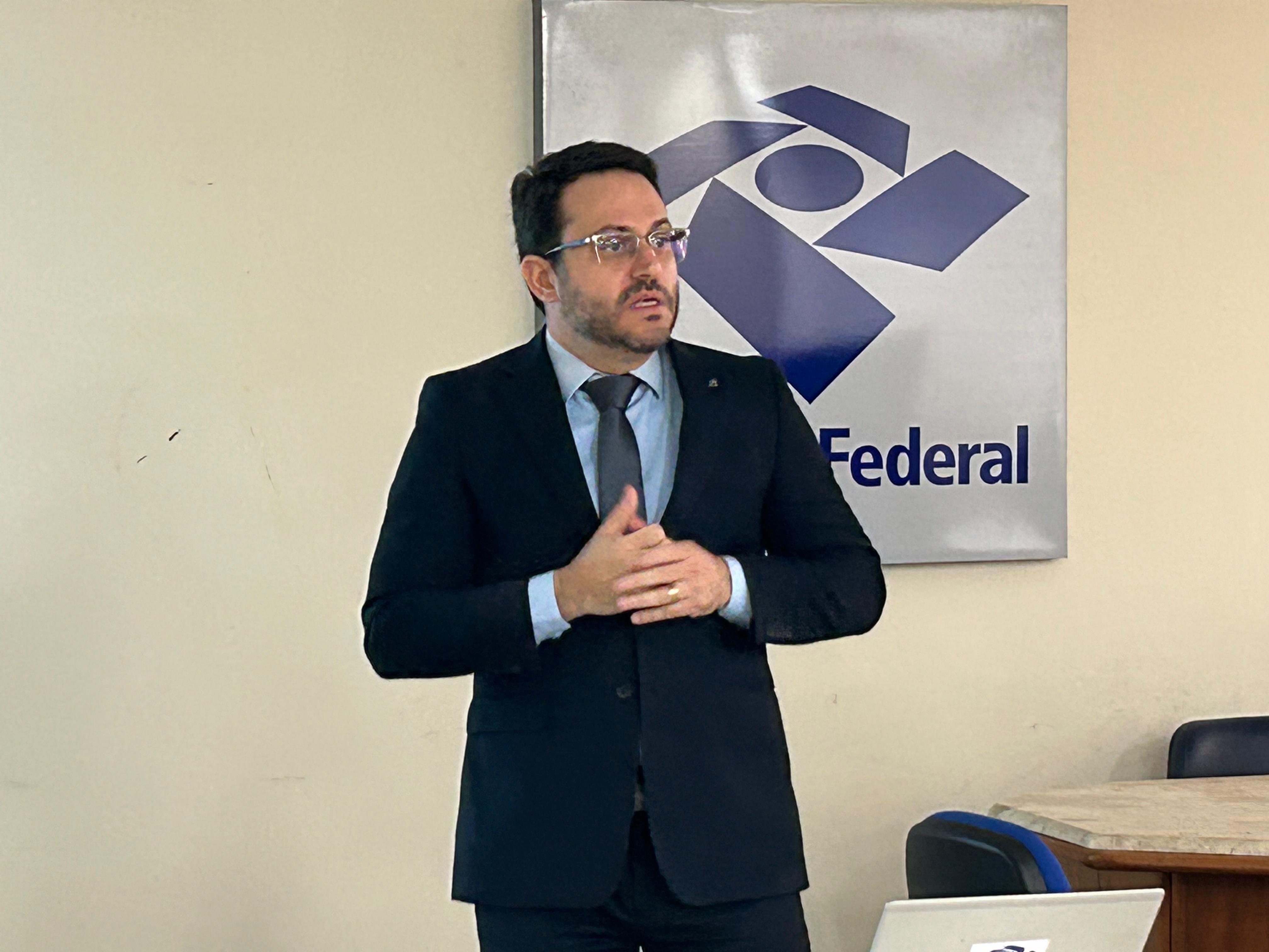 Delegado Ricardo, homem branco, cabelos escuros, usa óculos, terno escuro, camisa azul e gravata cinza 