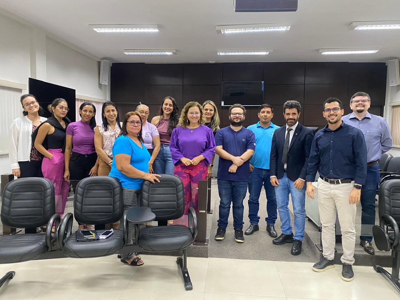 Homens e mulheres em pé formam roda de diálogo em sala de paredes brancas com persianas beges