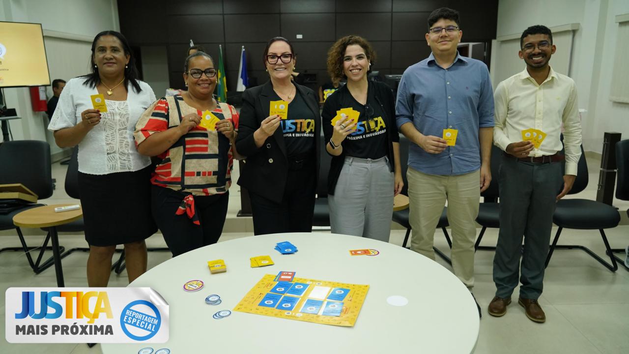 Homens e mulheres em foto posada numa sala de paredes laterais brancas e parede de madeira ao fundo